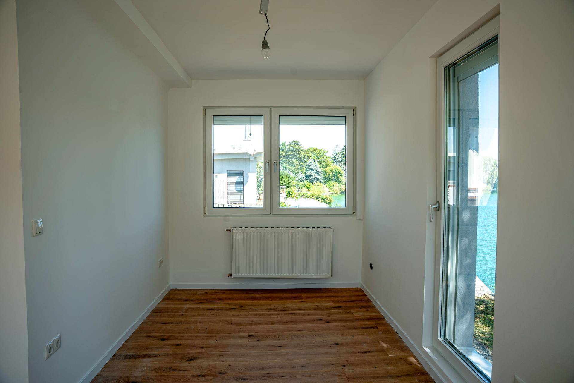 Heller Raum mit Holzboden und Blick auf den See durch große Fenster.