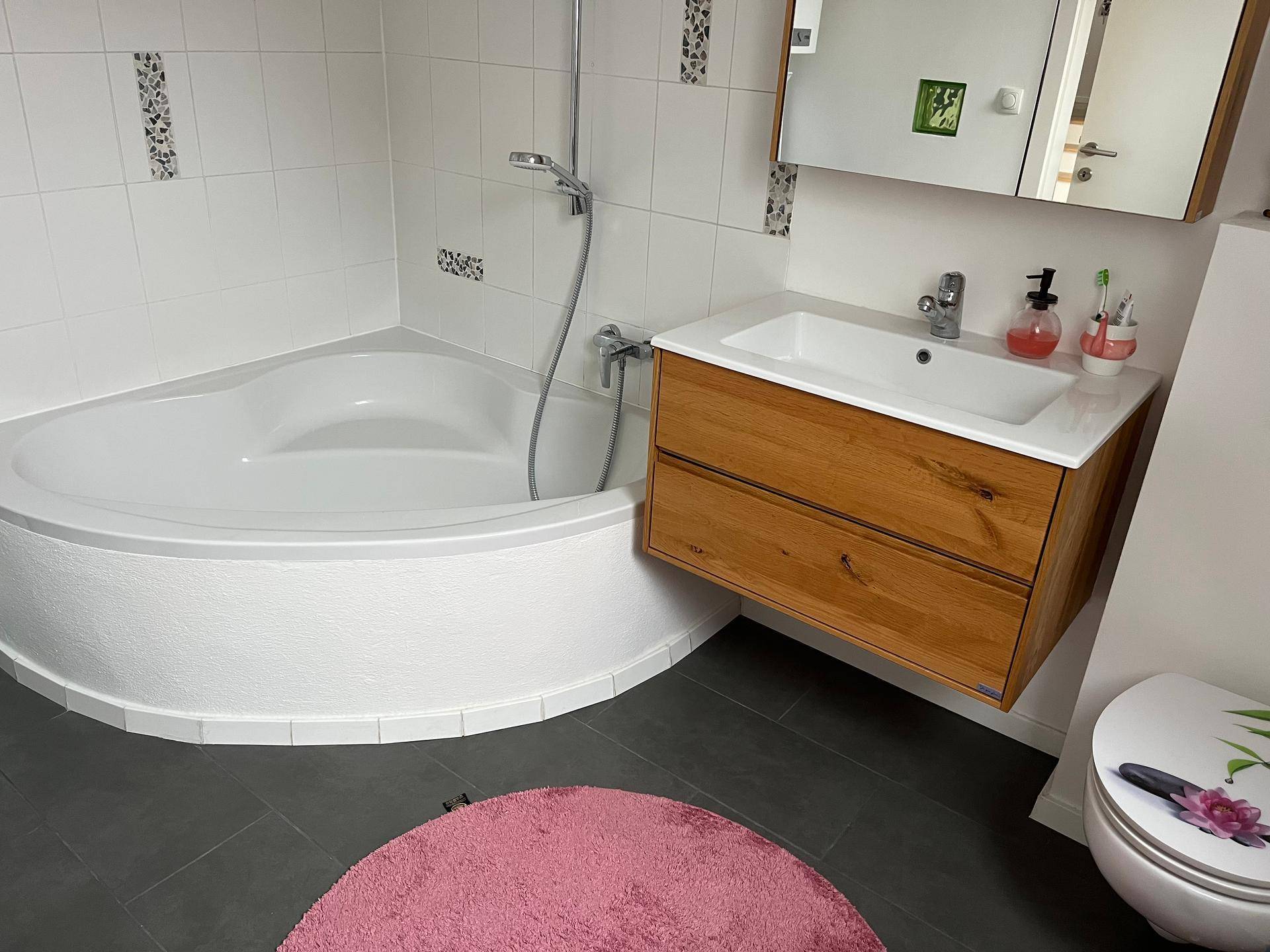 Modernes Badezimmer mit Eckbadewanne, Waschbeckenunterschrank und dunklen Bodenfliesen.