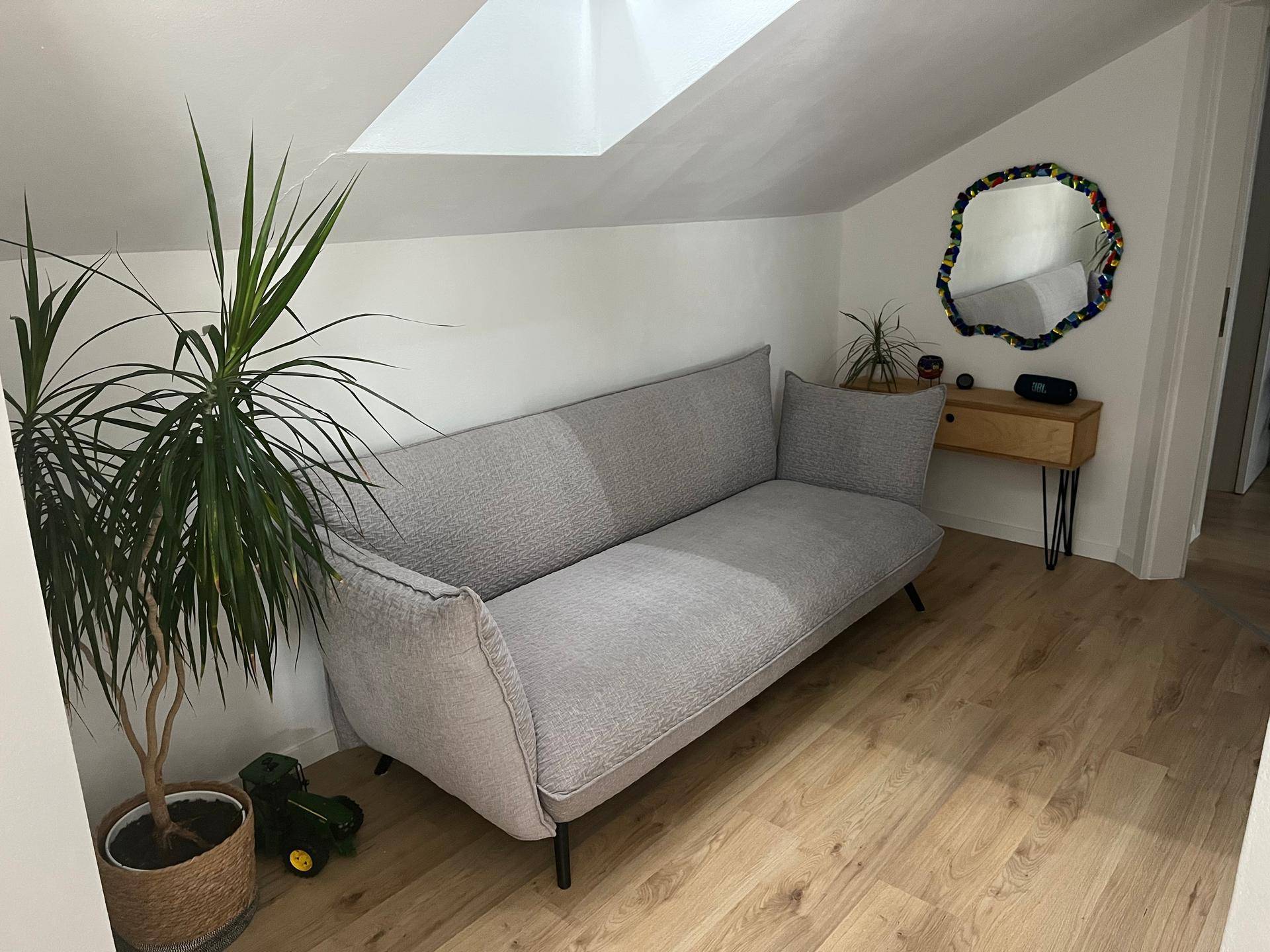 Heller Wohnbereich mit bequemer Couch, Pflanzen und schräger Decke mit Dachfenster.