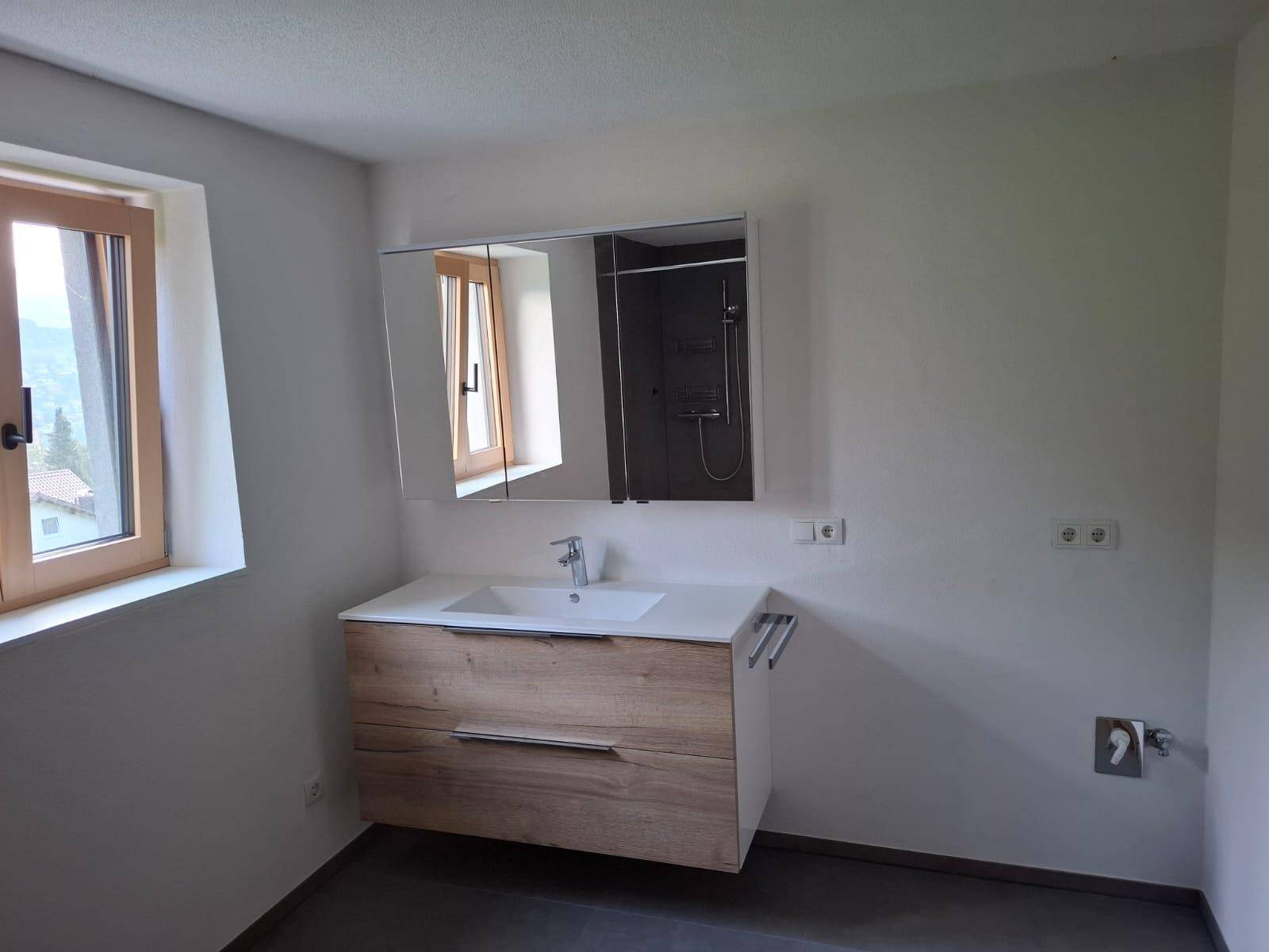 Modernes Badezimmer mit Holzwaschtisch, Spiegelschrank und Fenster für Tageslicht.