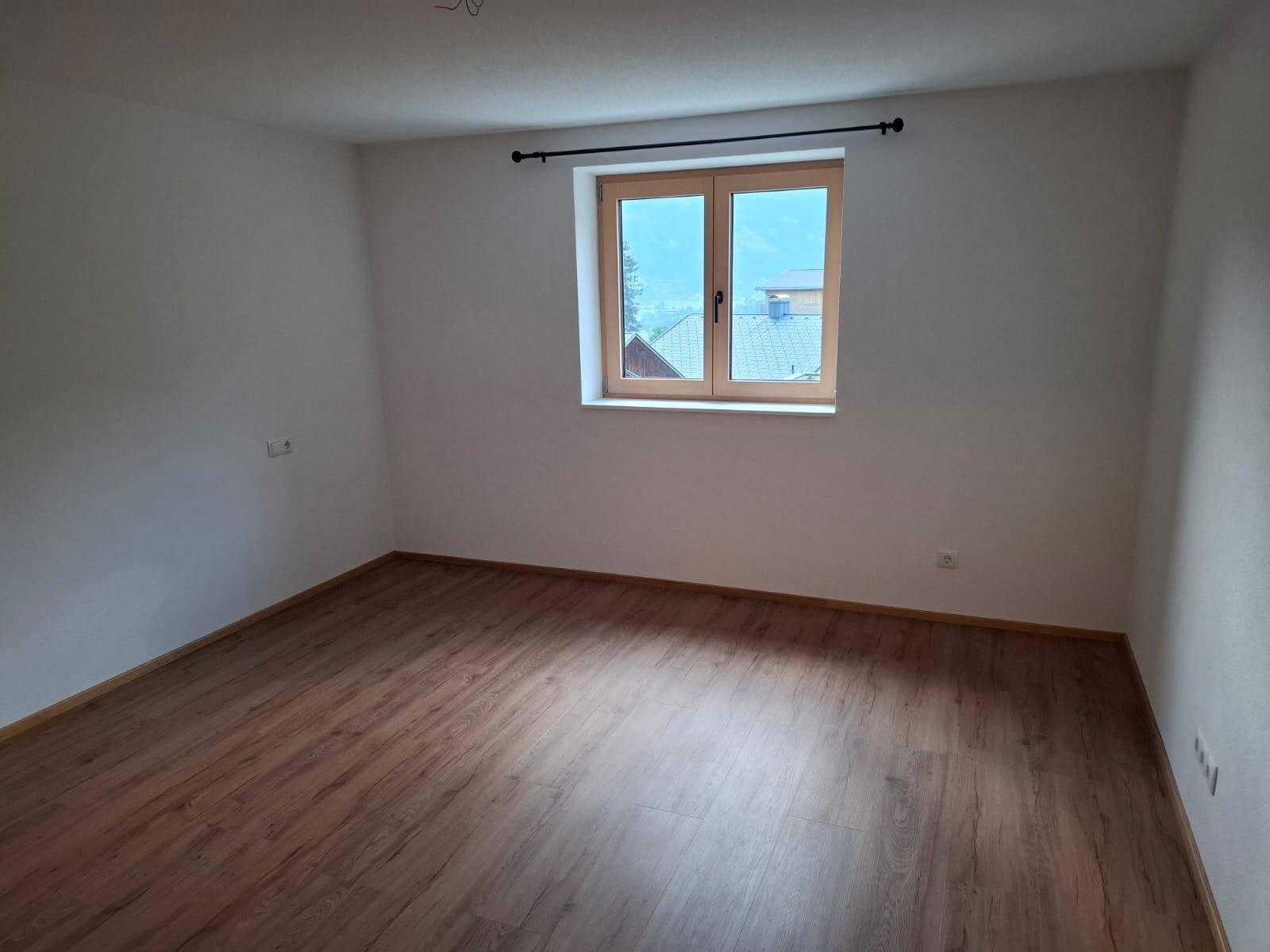 Geräumiges, leeres Zimmer mit Laminatboden und großem Fenster mit Fernblick.