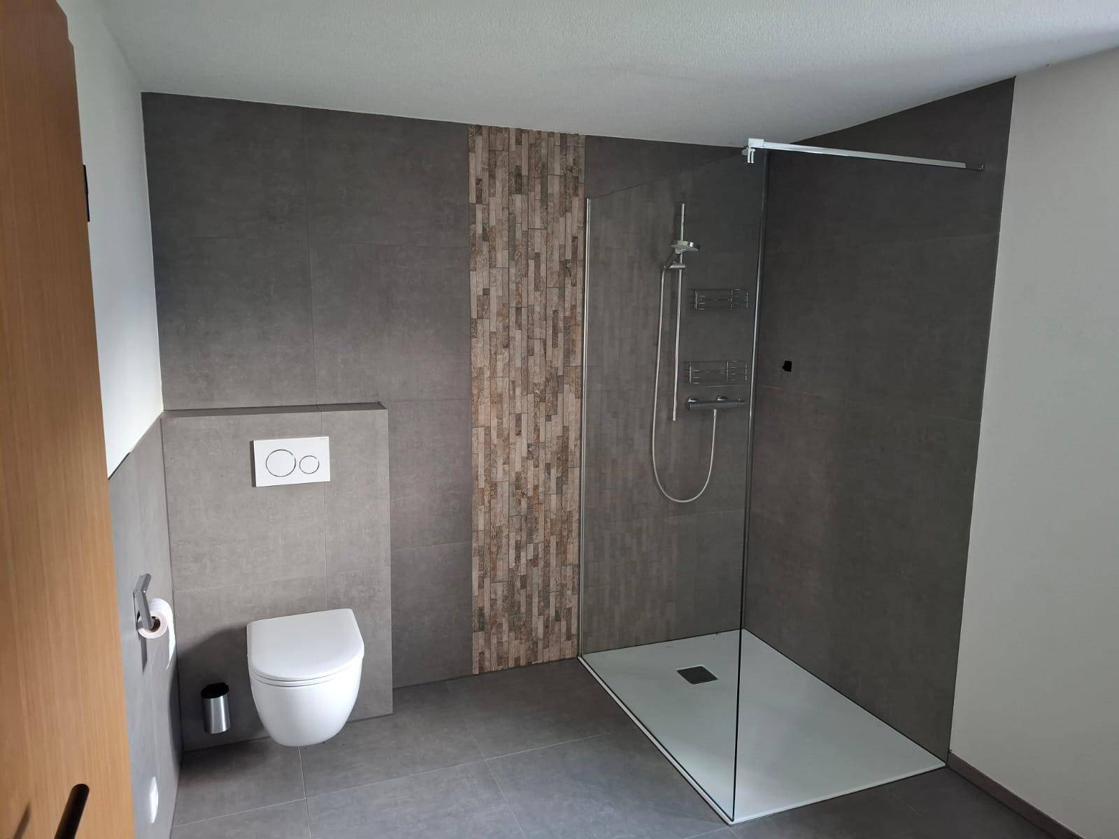 Zeitgemäßes Badezimmer mit großer begehbarer Dusche und wandhängendem WC in Grautönen.