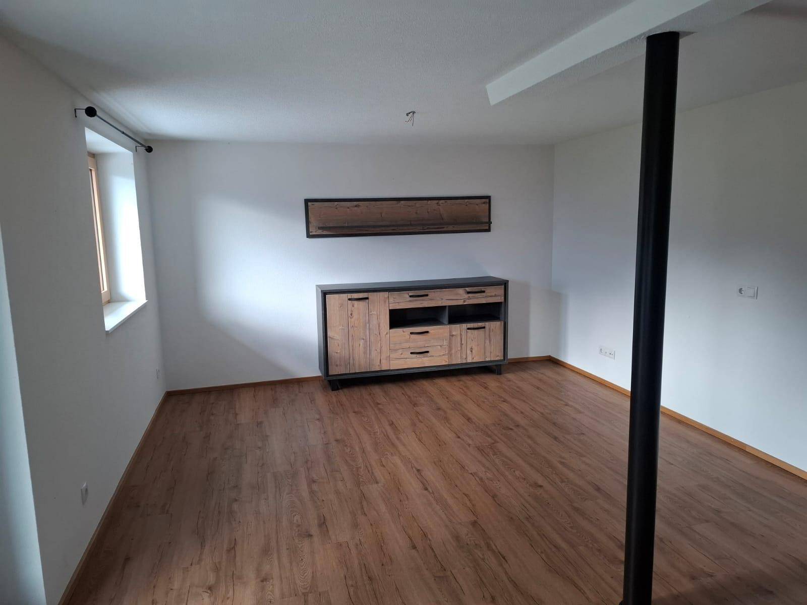 Heller Wohnbereich mit Laminatboden, modernem Sideboard und Fenster für natürliches Licht.