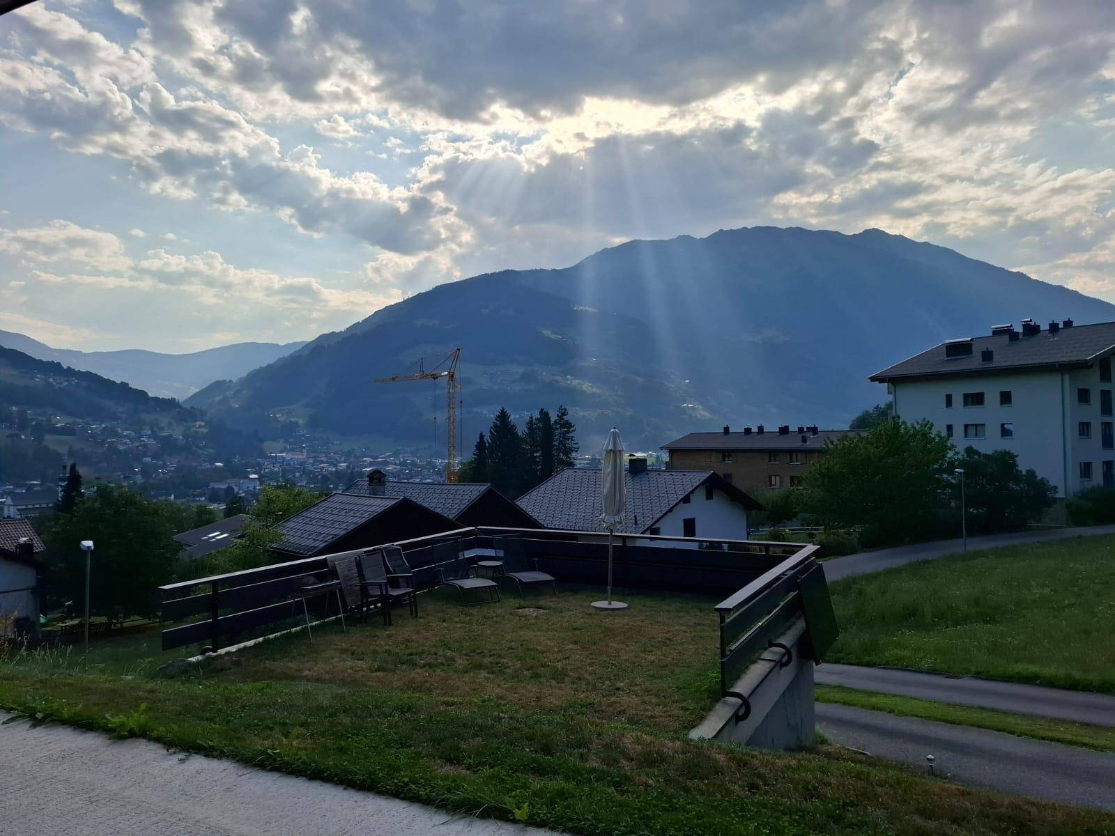 Grüne Gartenfläche mit Sitzgelegenheiten und beeindruckendem Bergblick unter bewölktem Himmel.