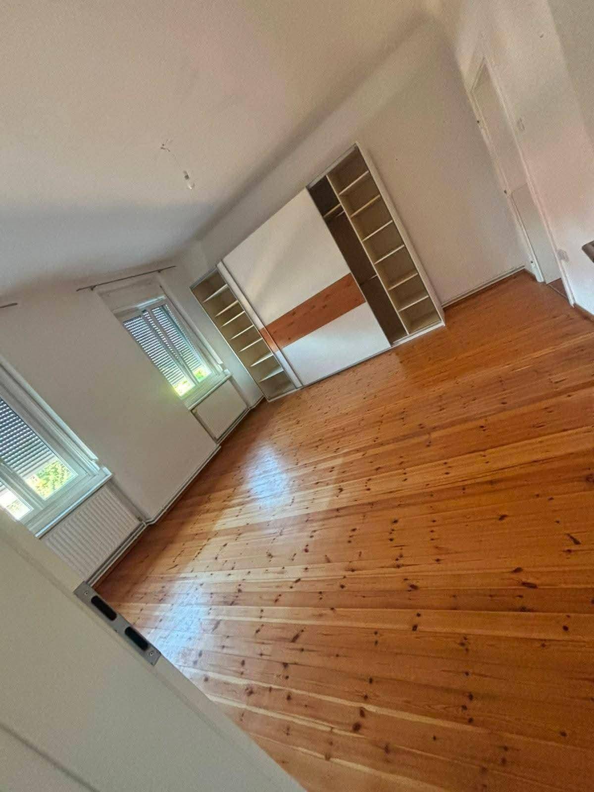 Helles Schlafzimmer mit Dielenboden, Einbauschrank und zwei Fenstern.