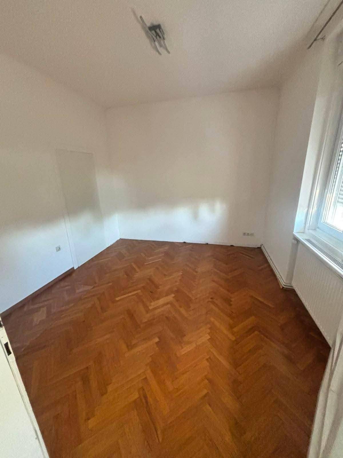 Leeres Schlafzimmer mit klassischem Fischgrätparkett und einem Fenster mit Jalousien.