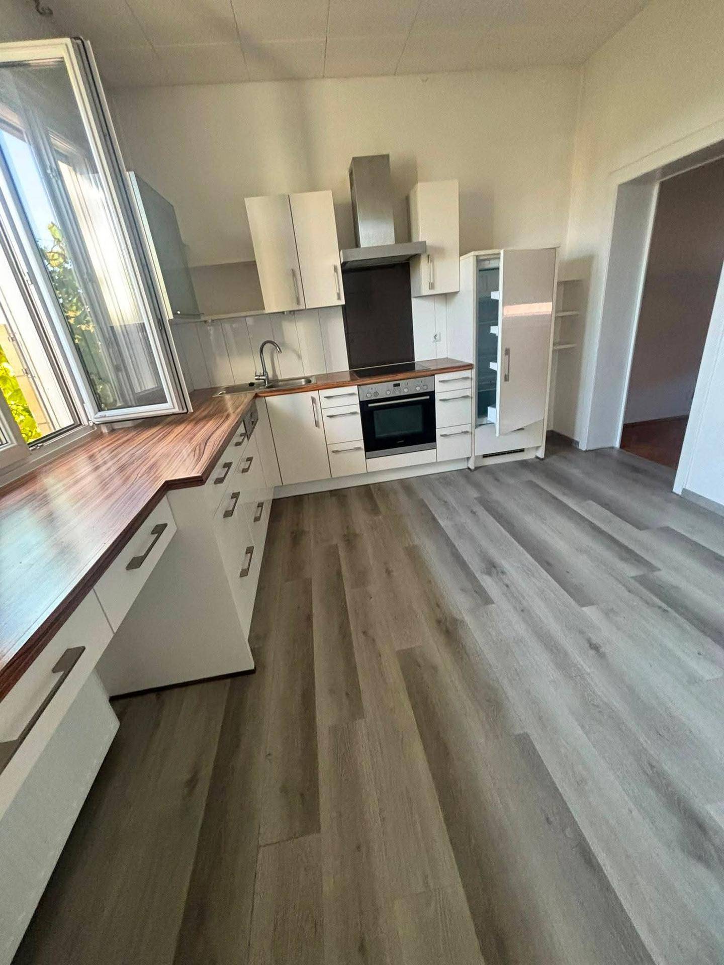 Funktionale Küche mit weißen Schränken, Holz-Arbeitsplatte und integriertem Backofen.