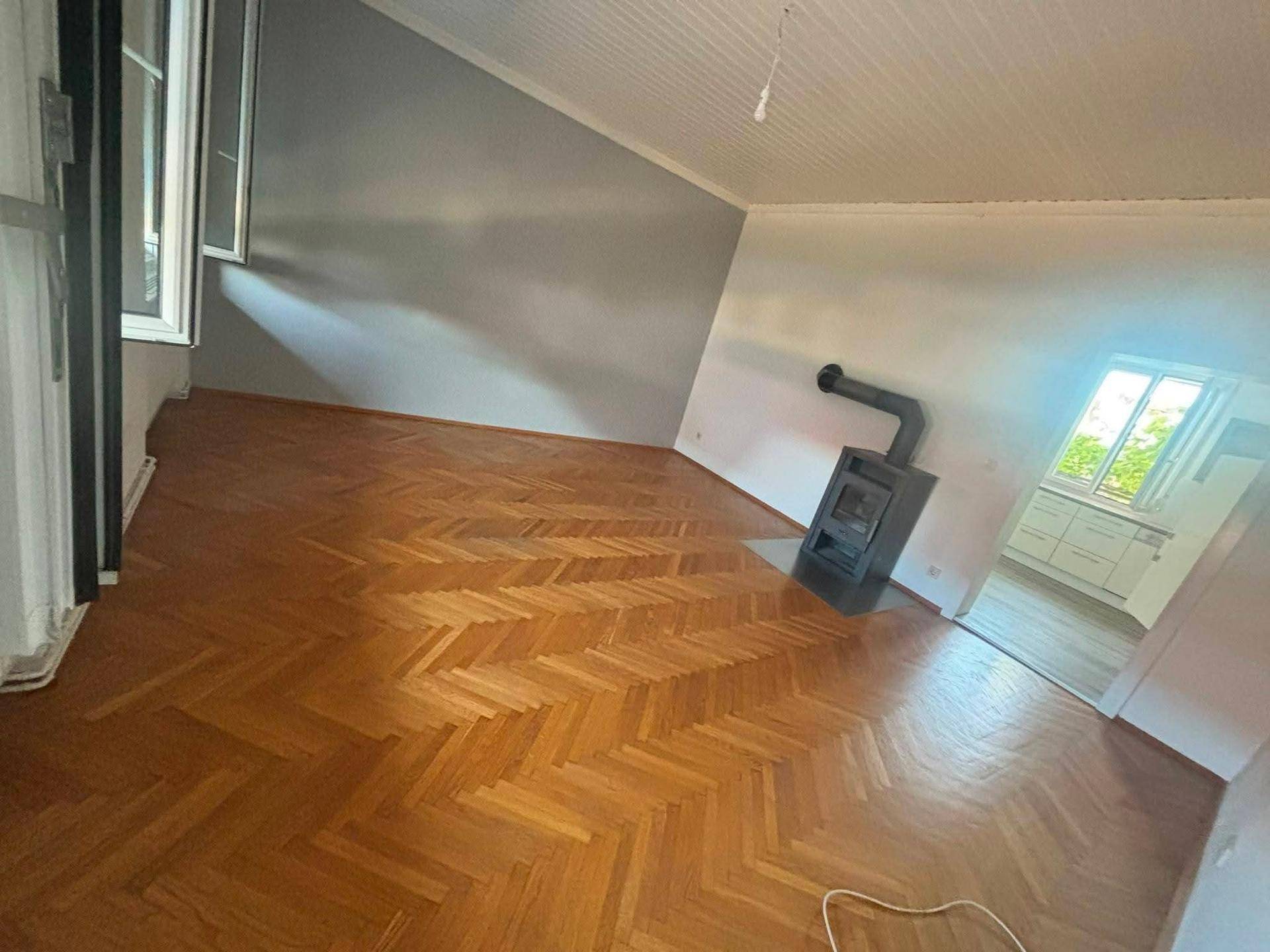 Gemütliches Wohnzimmer mit Fischgrätparkett, Dachschräge und einem Holzofen.