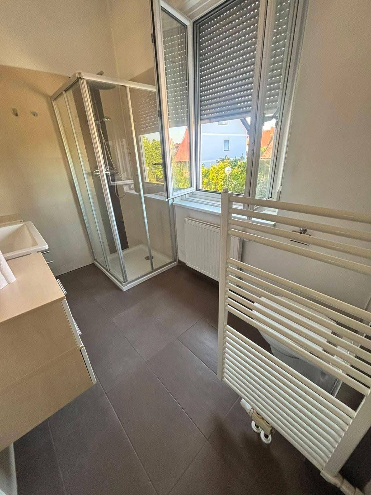Badezimmer mit Duschkabine, beheiztem Handtuchhalter und Fenster für Tageslicht.