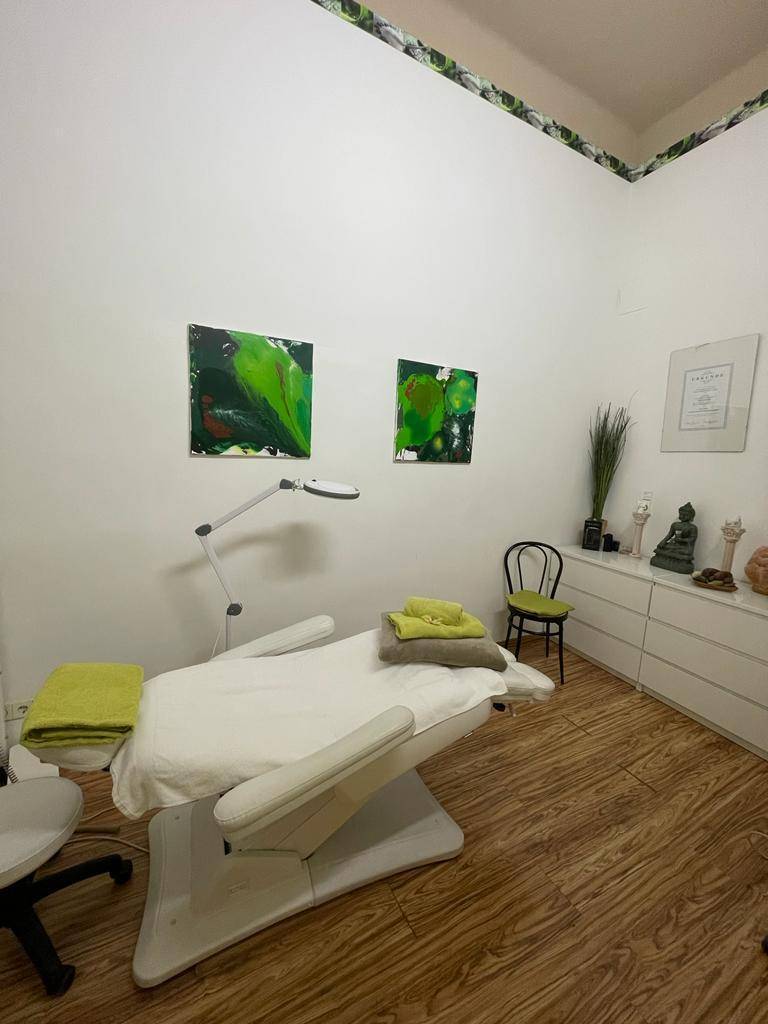 Behandlungsraum mit einer weißen Liege, grünen Handtüchern und passenden Kunstwerken an der Wand.