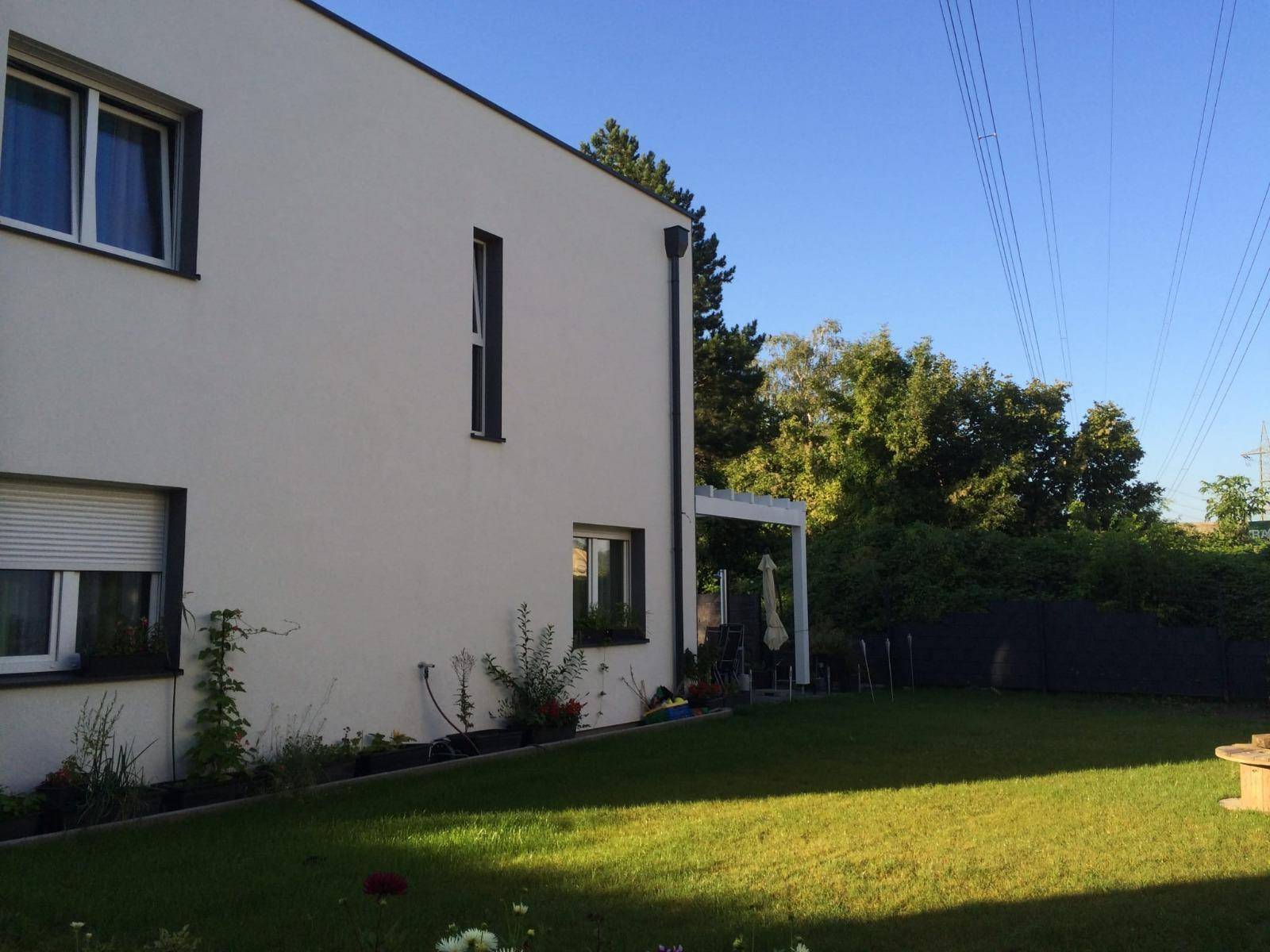 Modernes Einfamilienhaus mit gepflegtem Rasen und einer kleinen Terrasse unter blauem Himmel.