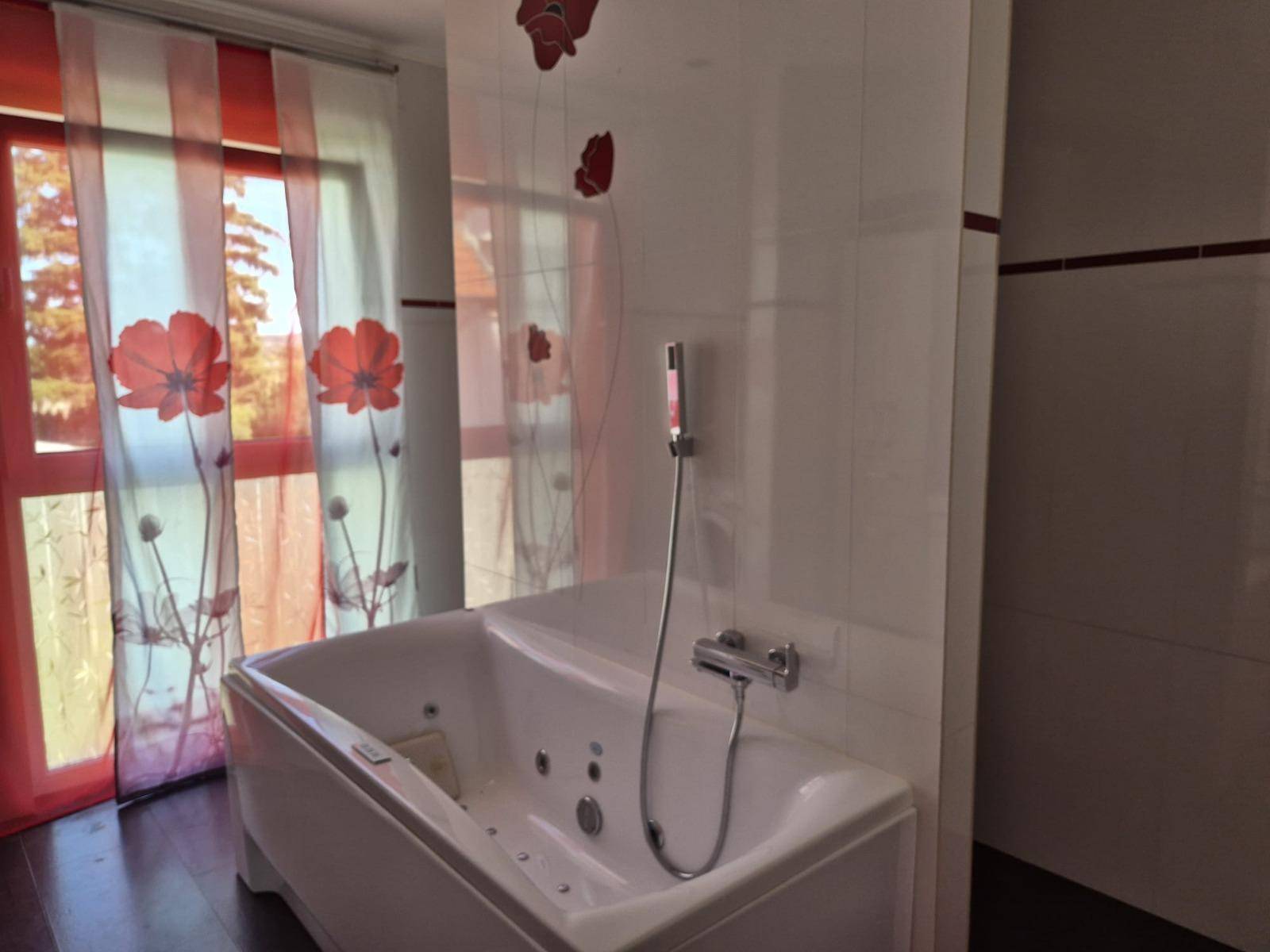 Badezimmer mit moderner Badewanne und farbenfrohen Vorhängen vor dem Fenster, das Tageslicht hereinlässt.