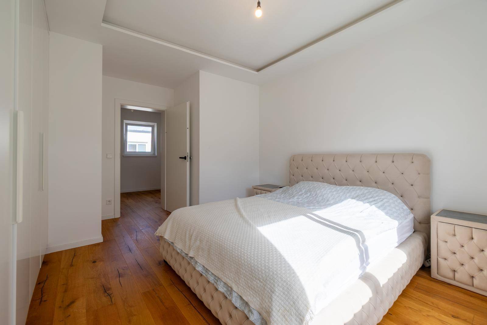 Schlafzimmer mit bequemem Polsterbett, Holzboden und indirekter Deckenbeleuchtung.