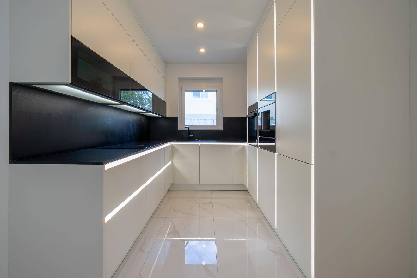 Moderne Küche mit weißen Schränken, schwarzen Arbeitsplatten und integrierter LED-Beleuchtung.