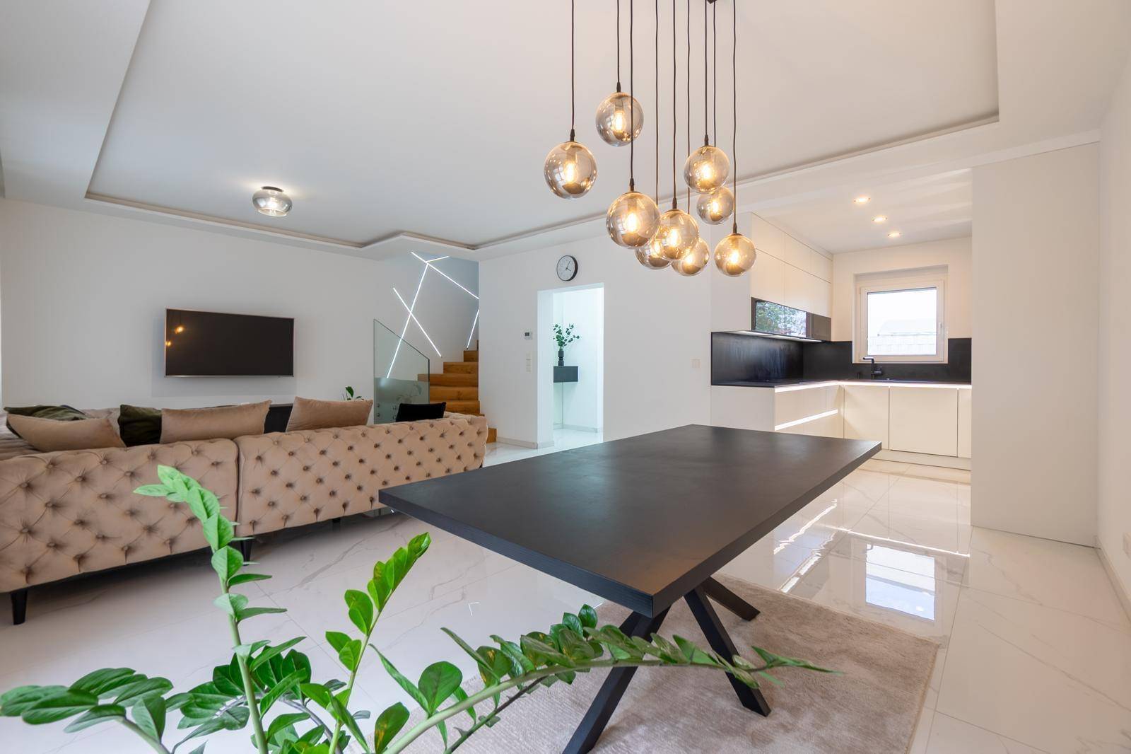 Geräumiger Wohn- und Essbereich mit großem Esstisch, beigem Sofa und Blick zur Küche.