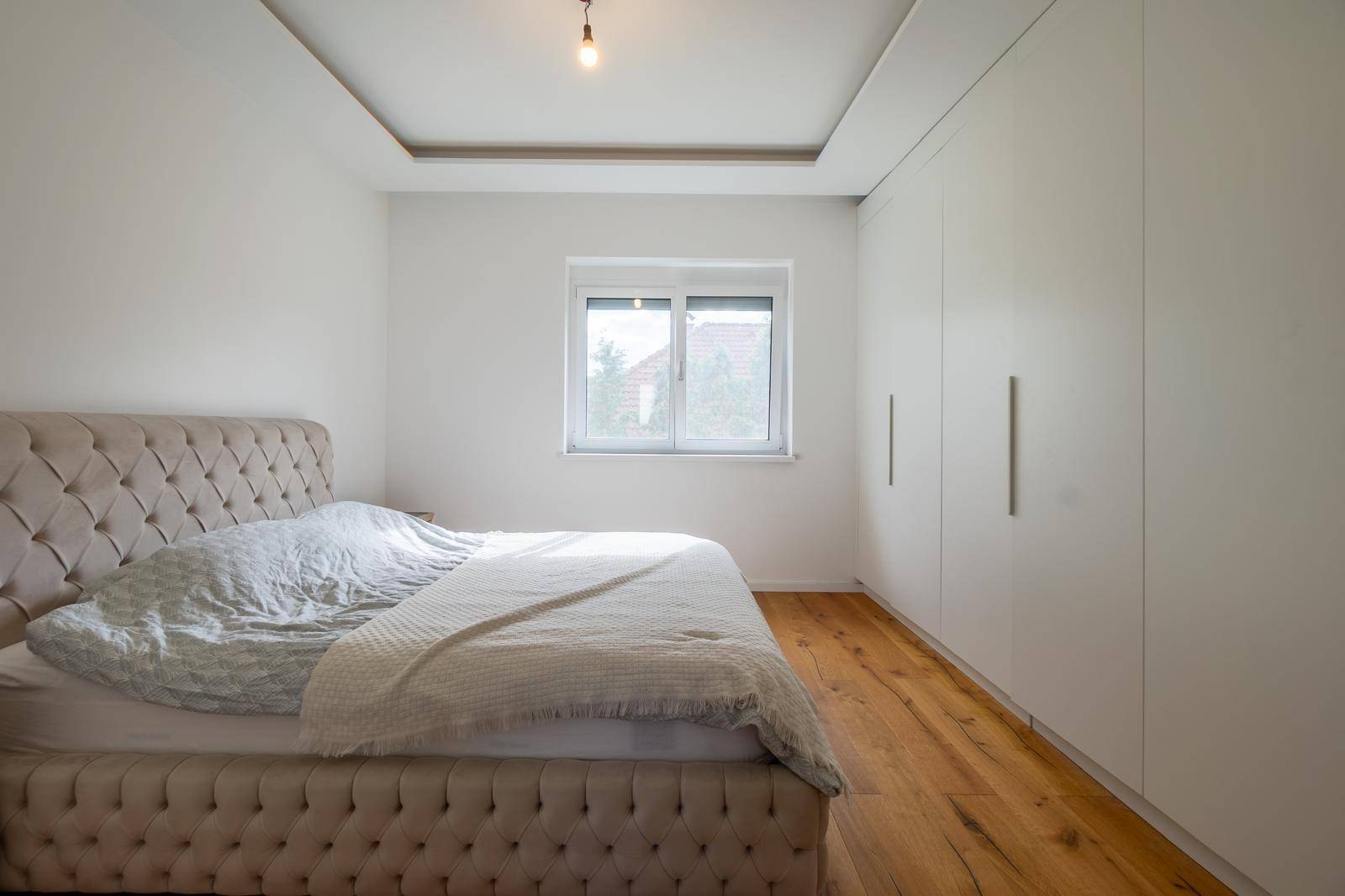 Schlafzimmer mit großem Fenster, Holzboden und Einbauschränken entlang einer Wand.