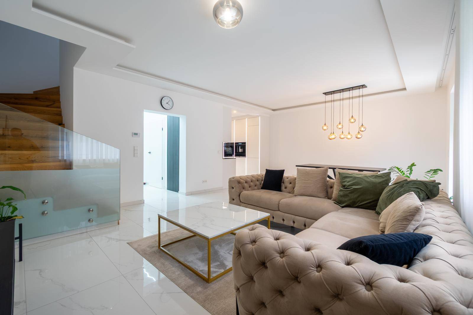Gemütliches Wohnzimmer mit großem Ecksofa, Couchtisch und Treppenaufgang mit Glasgeländer.