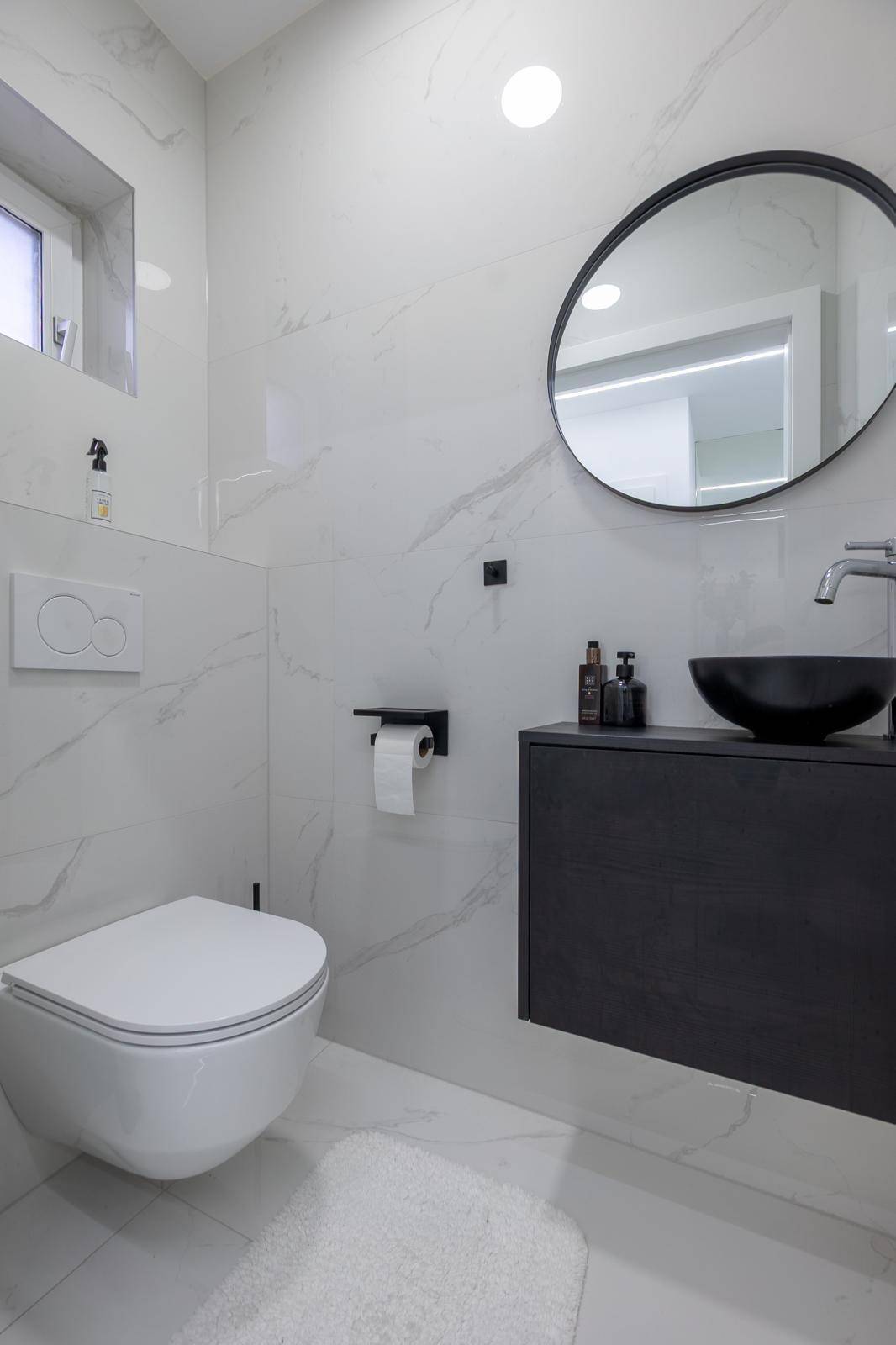 Modernes Gäste-WC mit Wand-WC, schwarzem Waschtisch und rundem Spiegel.