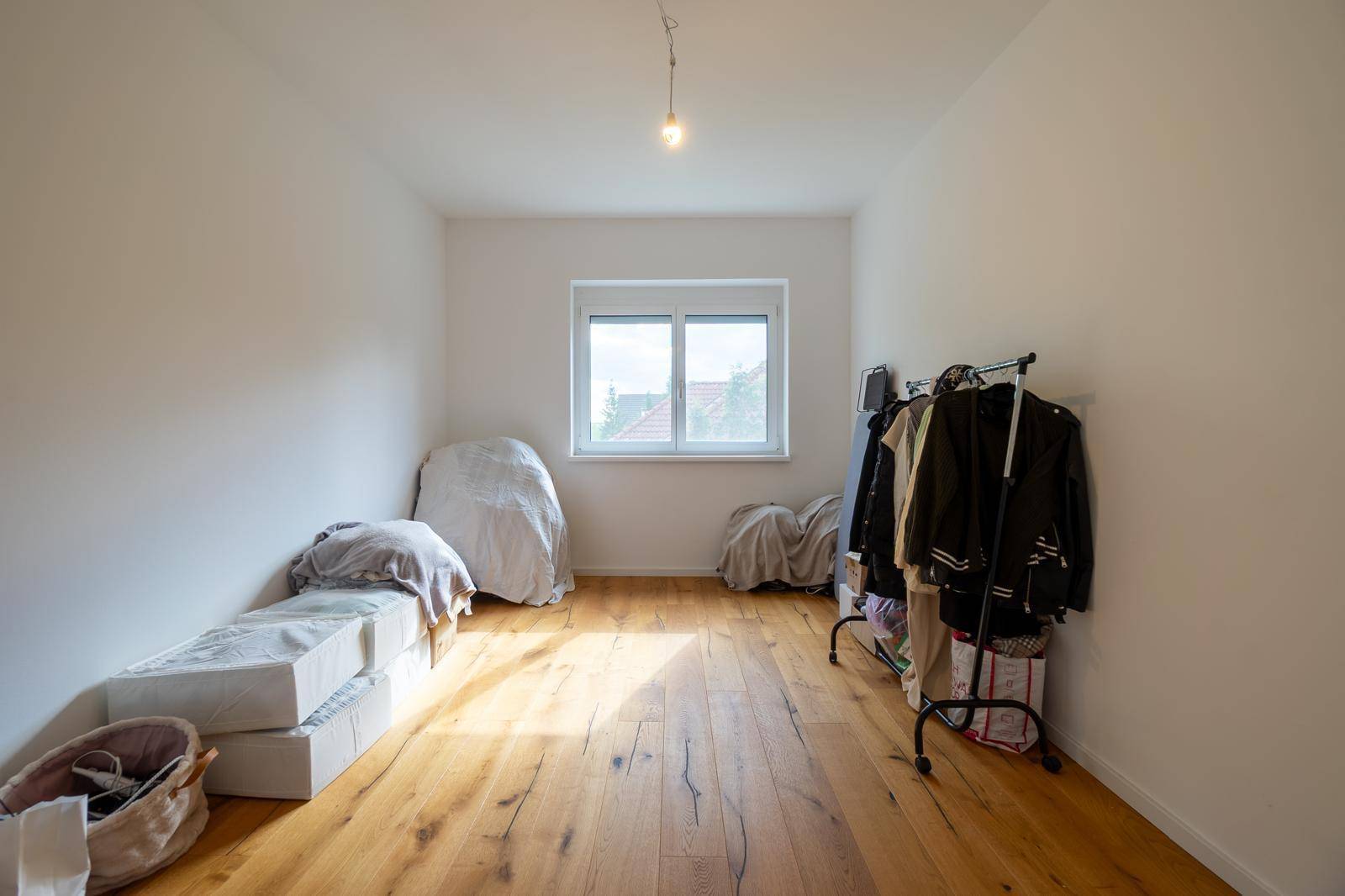 Helles Schlafzimmer mit Holzboden und Fenster, das viel natürliches Licht hereinlässt.
