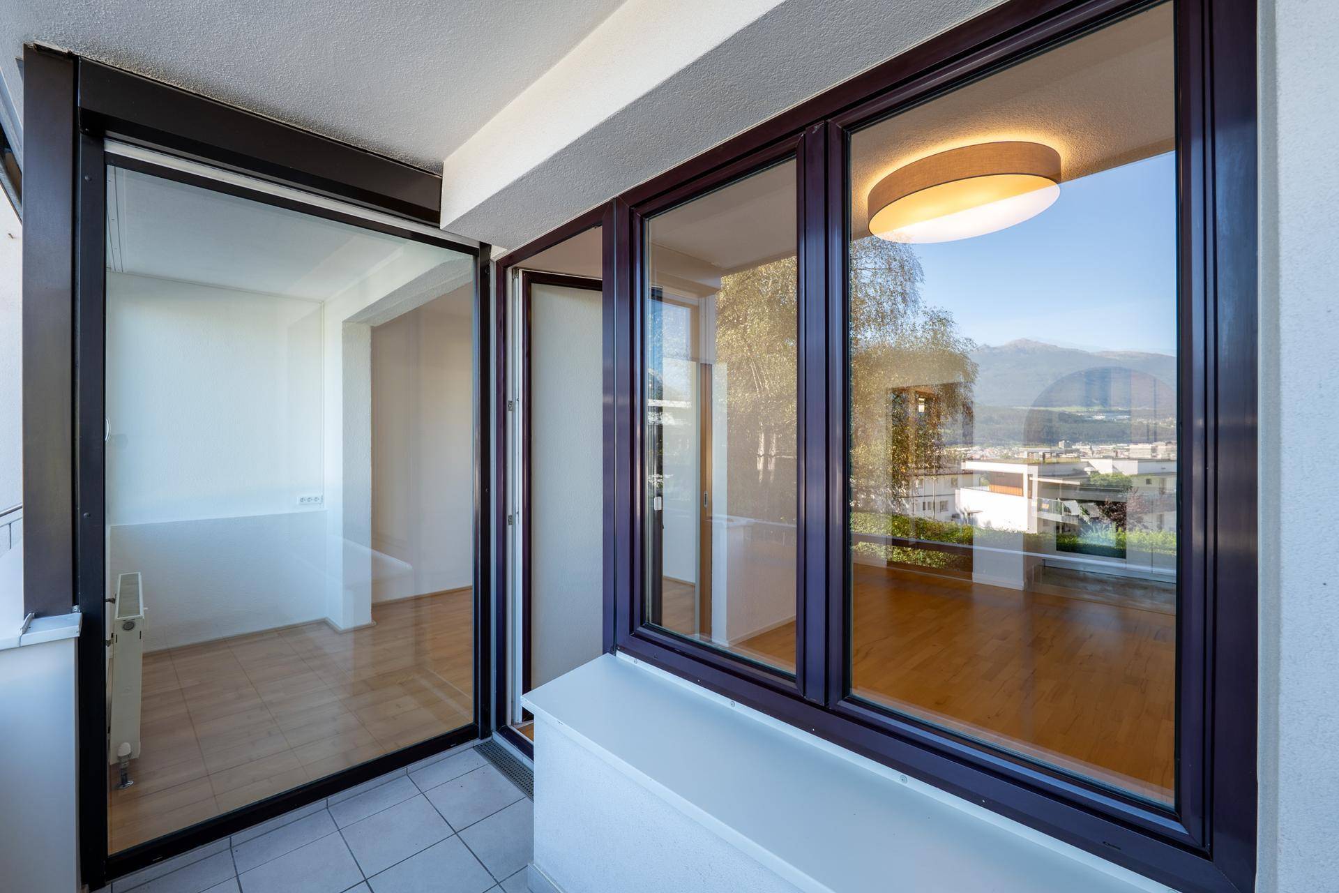 Balkon mit Fliesenboden und Blick in den hellen Innenraum mit Holzboden.
