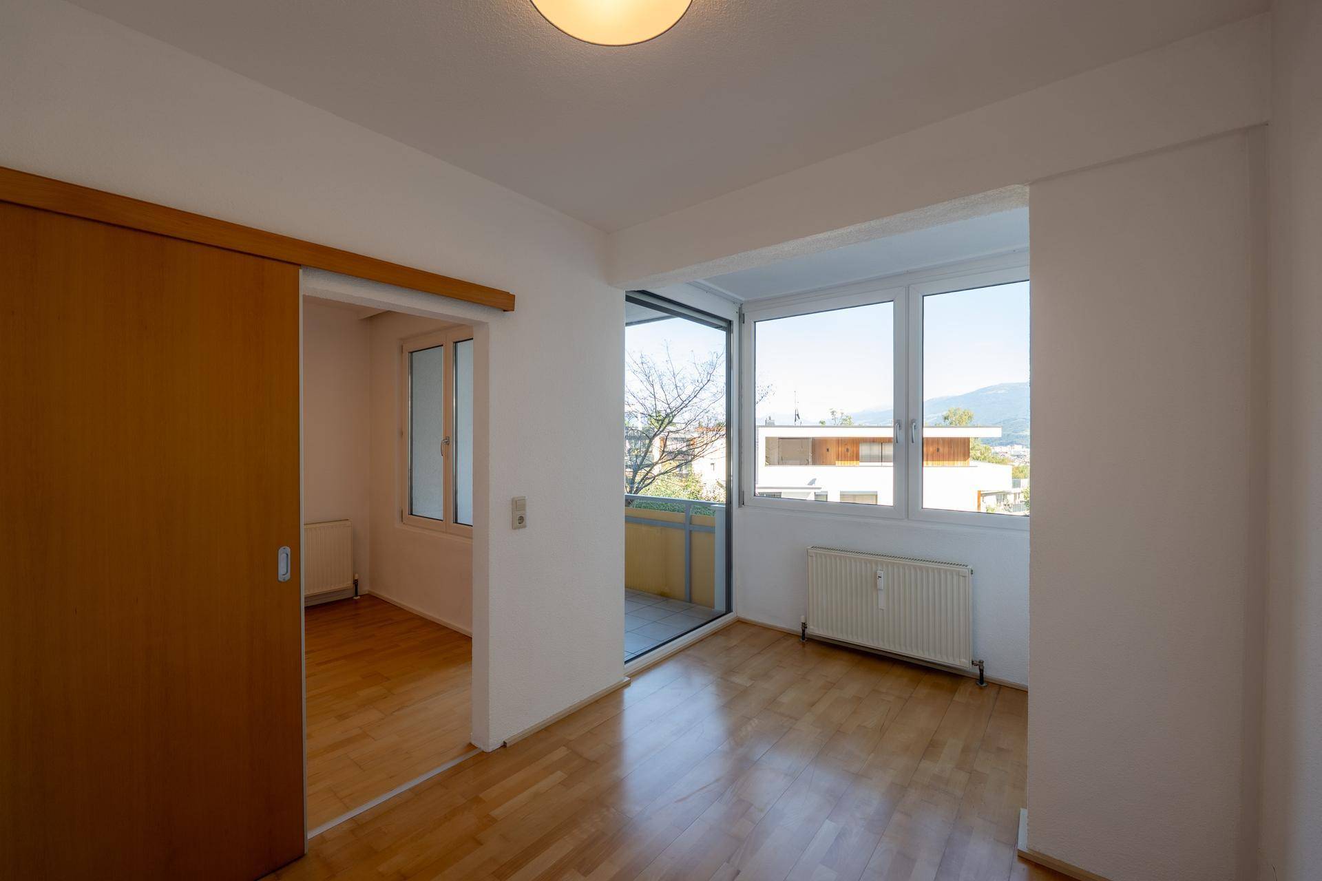 Helles Zimmer mit Holzboden, Schiebetür und Zugang zu einem Balkon mit Aussicht.