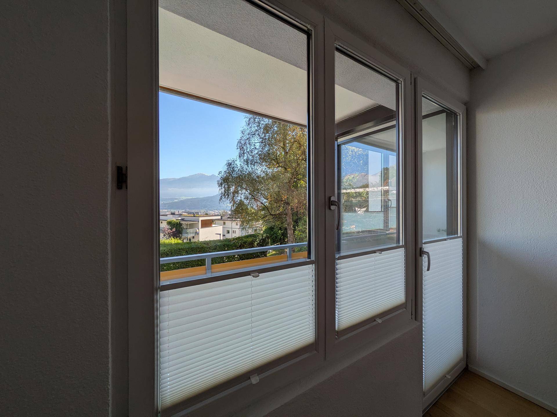 Innenansicht mit großen Fenstern und Balkontür, die einen weiten Blick auf die Landschaft freigeben.