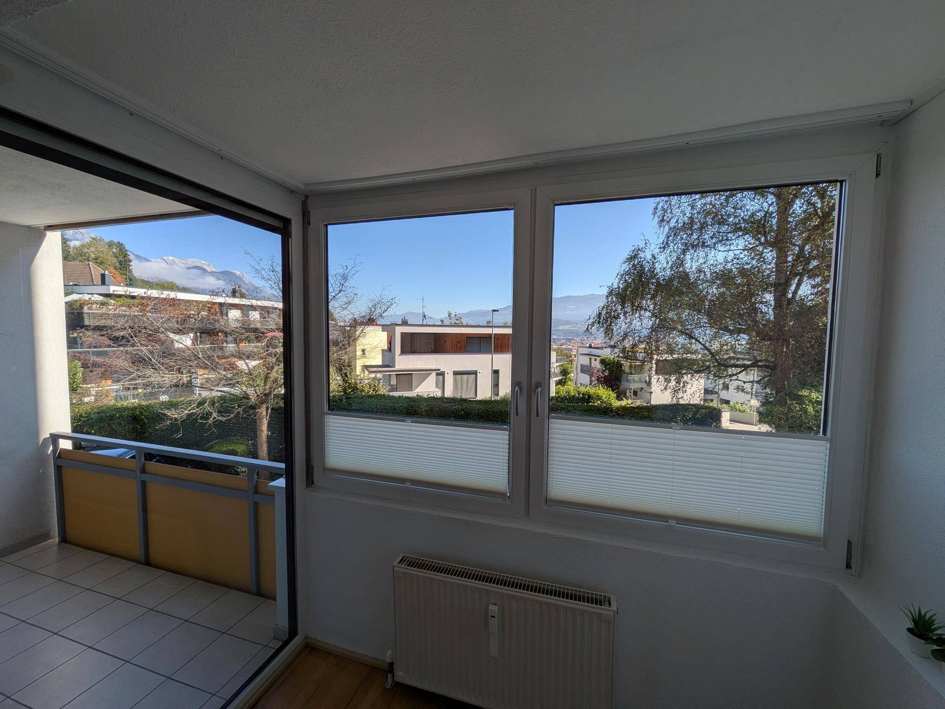 Heller Innenraum mit Fenster und Balkonzugang, bietet Blick auf die Umgebung und Berge.