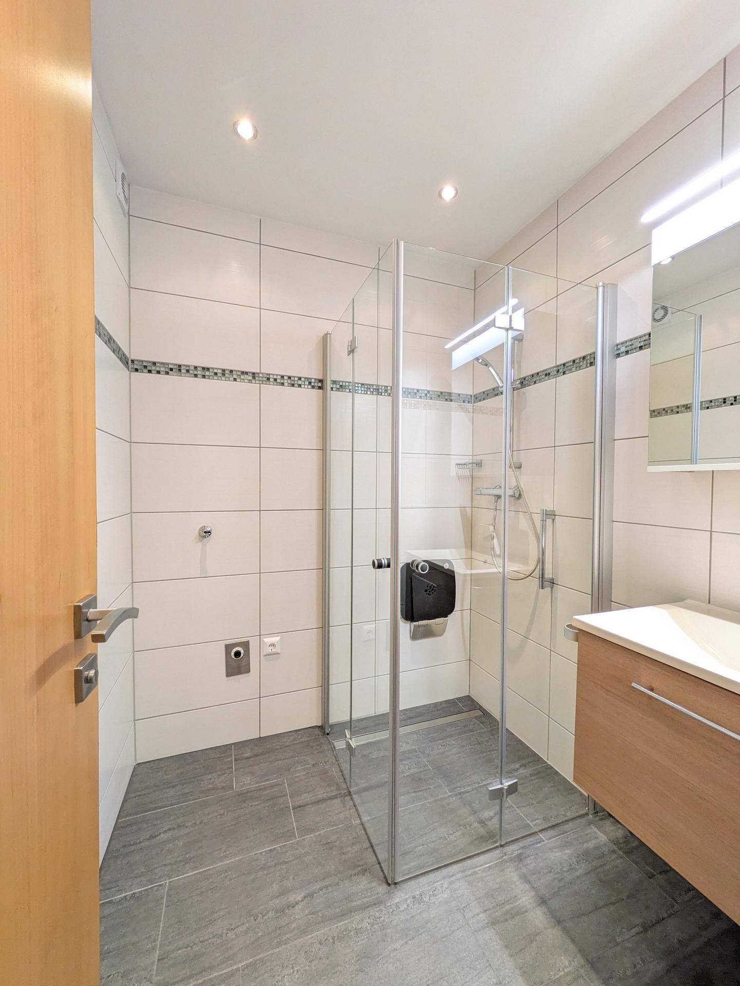 Modernes Badezimmer mit weißen Fliesen, begehbarer Dusche und Holzwaschtisch.