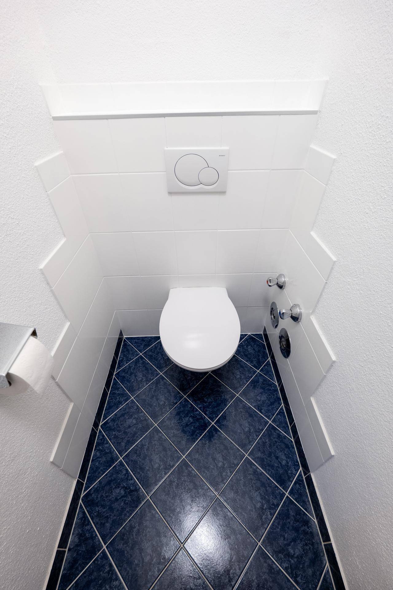Kleines WC mit wandhängender Toilette und dunkelblau gefliestem Boden.