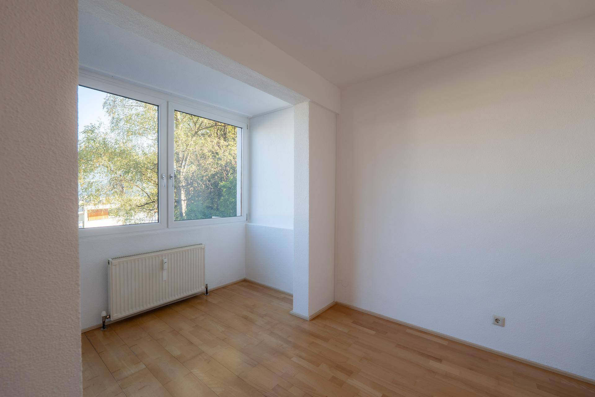 Ruhiges Zimmer mit Holzboden, großen Fenstern und viel Tageslicht.