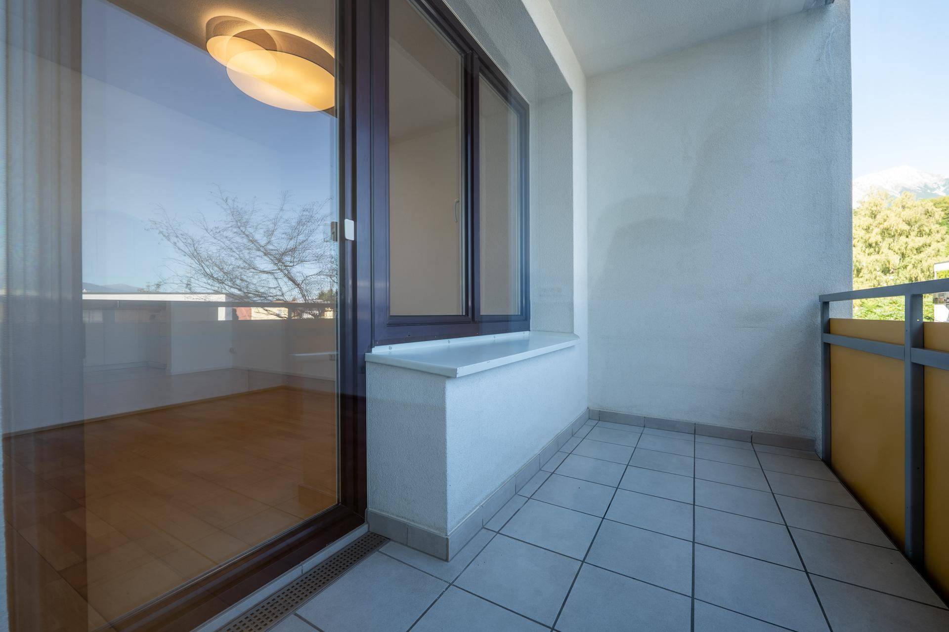 Heller Balkon mit Fliesenboden und Zugang zu einem Innenraum mit Holzboden.