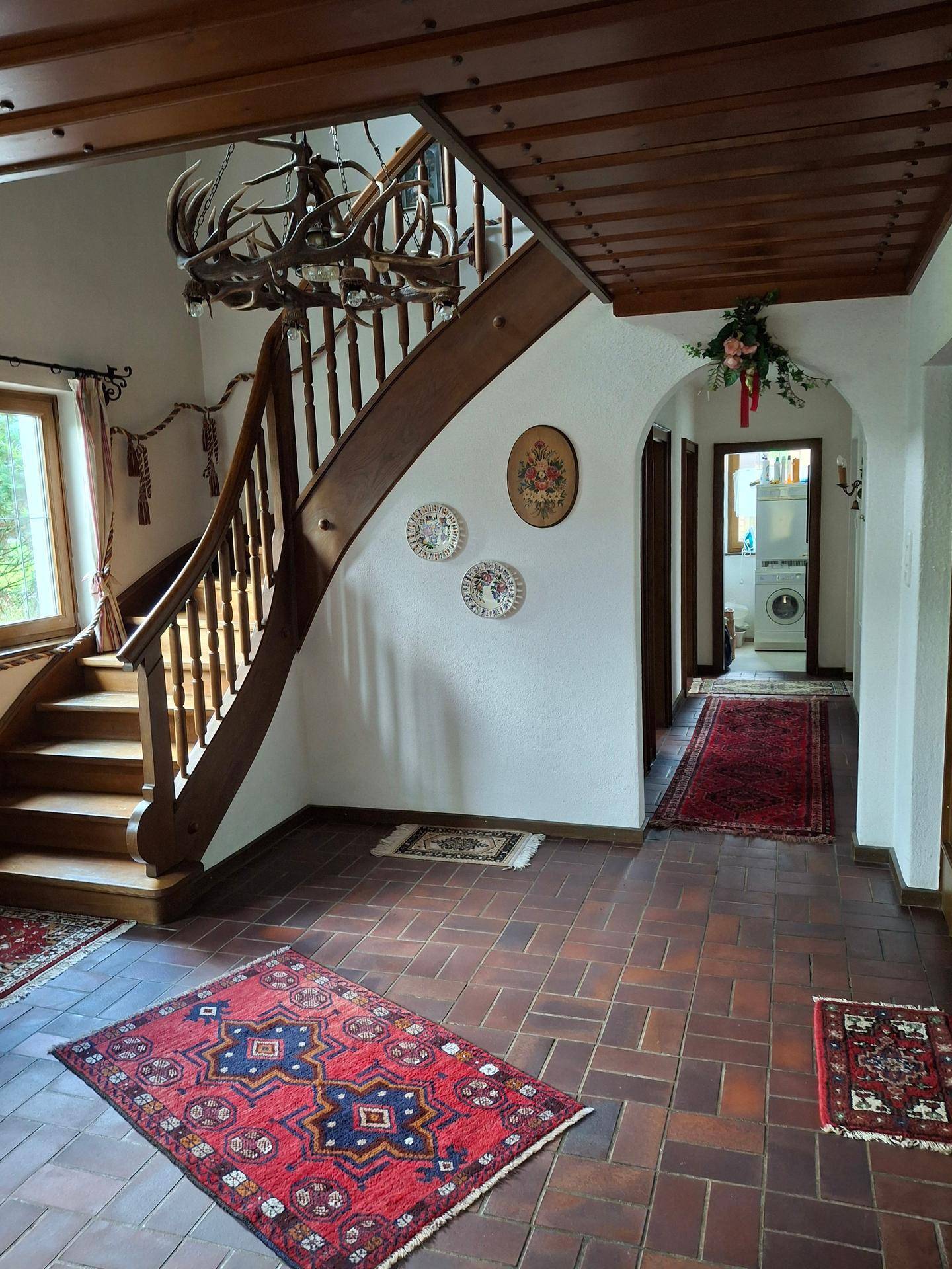 Geräumiger Eingangsbereich mit Holztreppe, Fliesenboden und traditioneller Hirschgeweih-Beleuchtung.