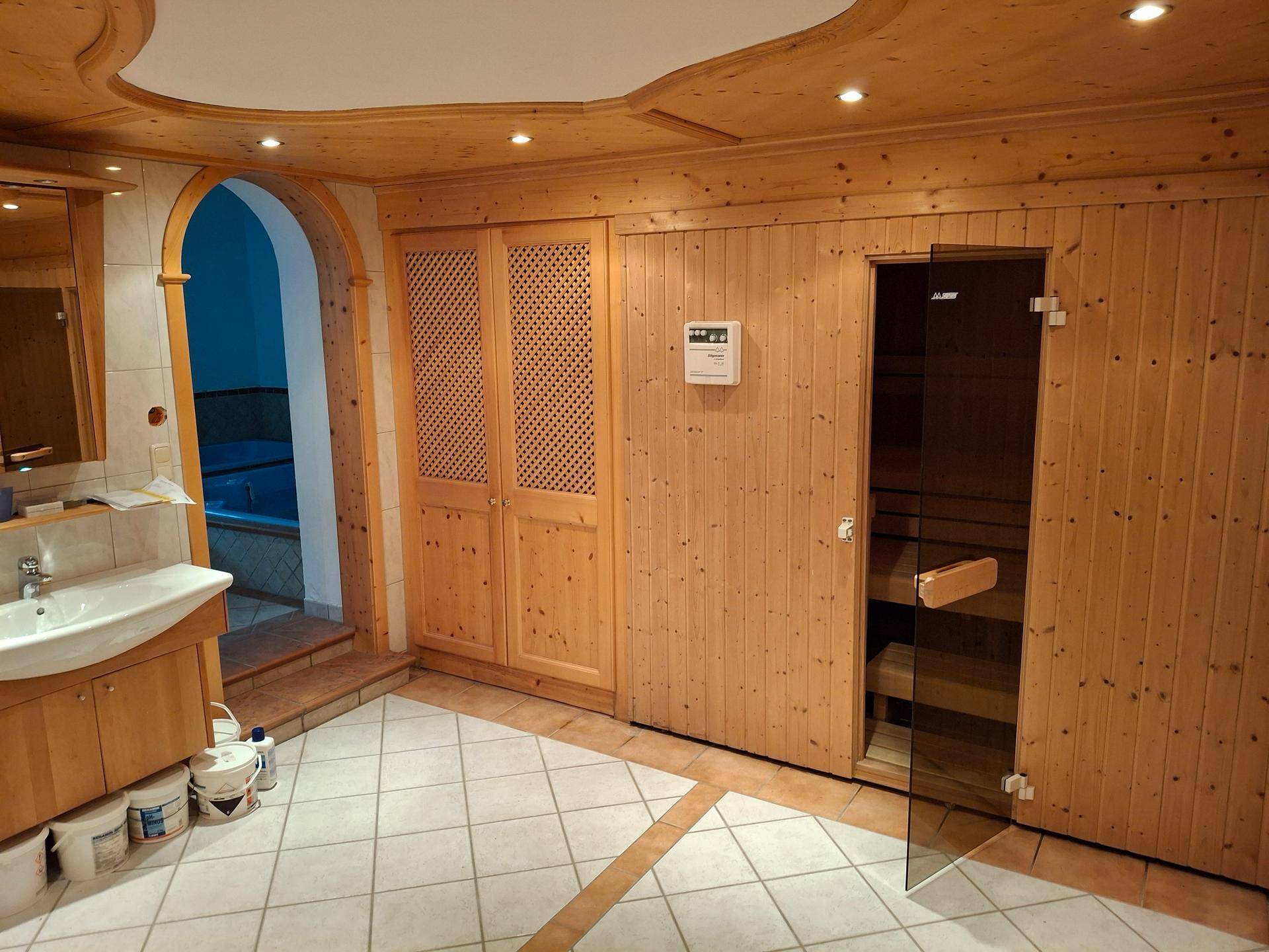 Wellnessbereich mit Holzvertäfelung, Sauna, Waschbecken und Zugang zu einem Whirlpool.