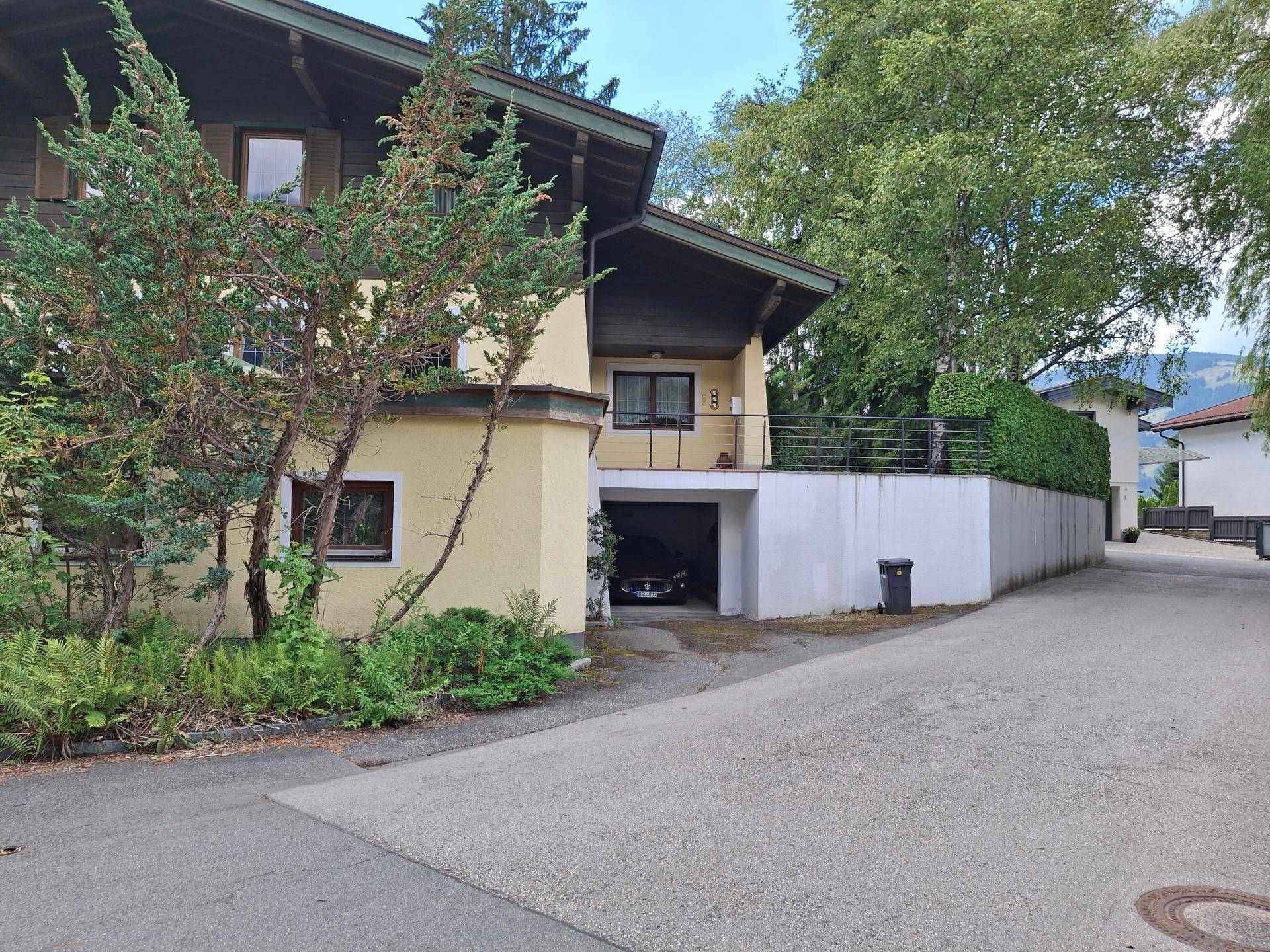 Seitenansicht des Hauses mit integrierter Garage, Auffahrt und üppiger Bepflanzung.