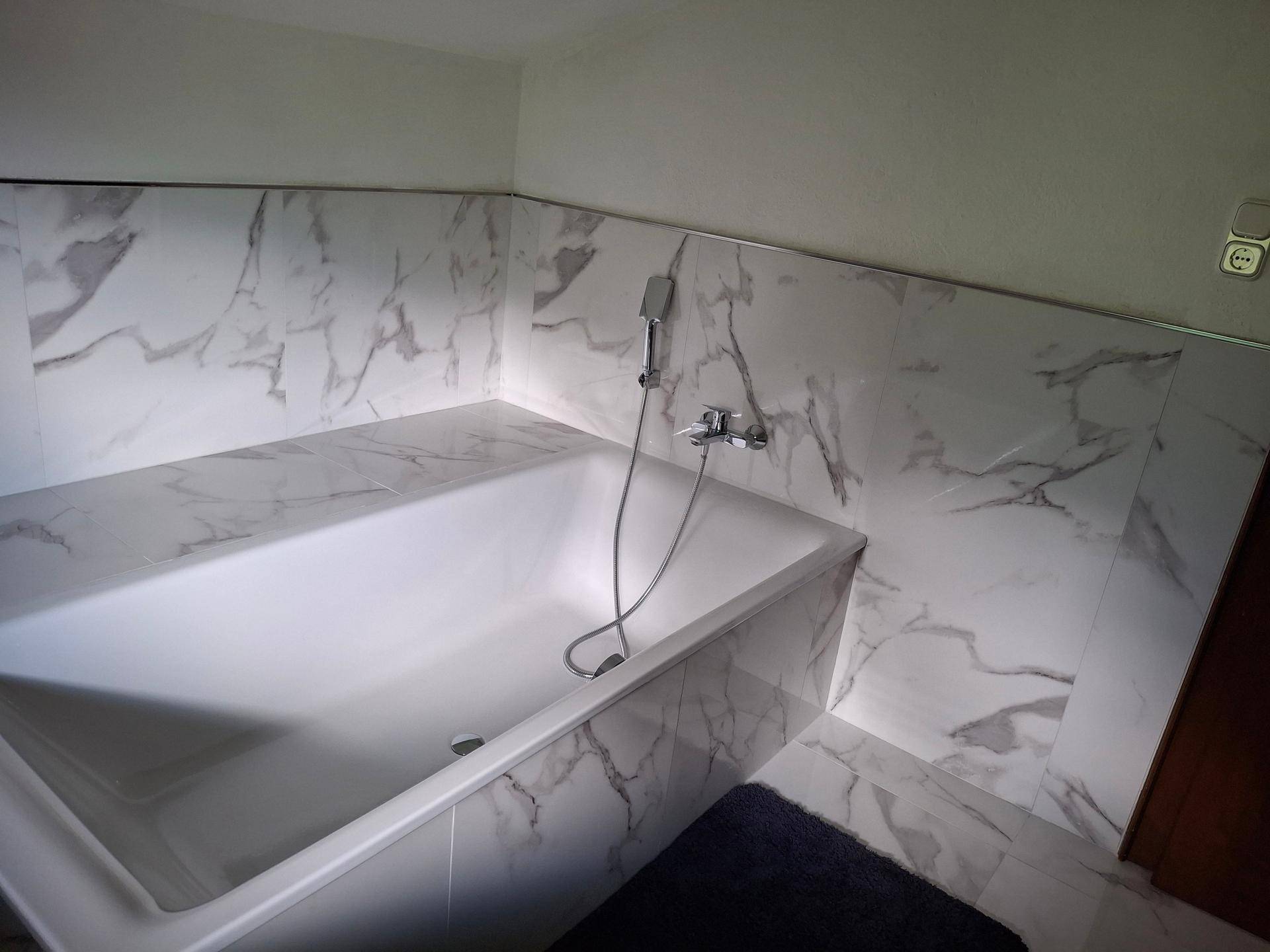 Badezimmer mit eingebauter Badewanne und eleganten Fliesen in Marmoroptik.