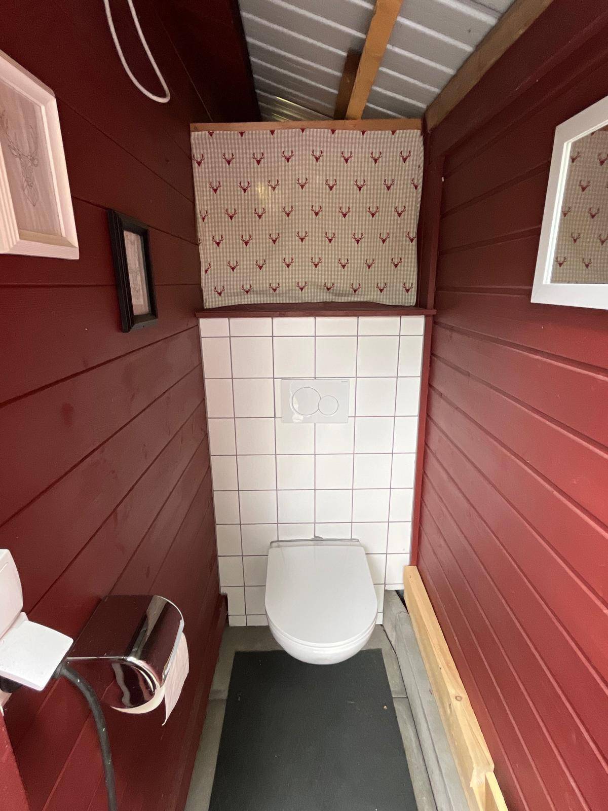 Kleines WC im Inneren des Gartenpavillons mit roten Holzwänden und weiß gefliestem Bereich.