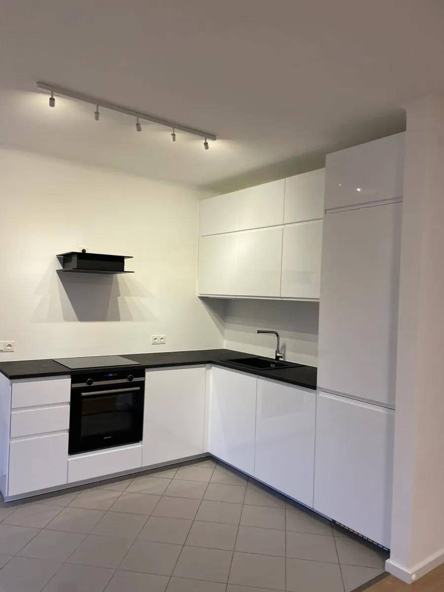 Weiße Hochglanzküche mit integriertem Backofen und Induktionskochfeld, ideal für modernes Wohnen.