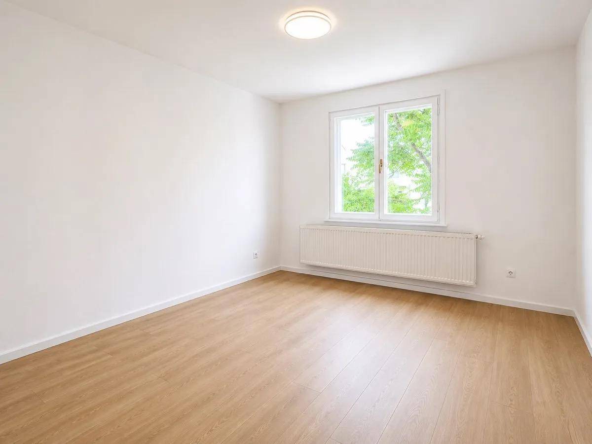 Freundliches Zimmer mit Holzboden und Fenster, das einen angenehmen Blick ins Grüne bietet.