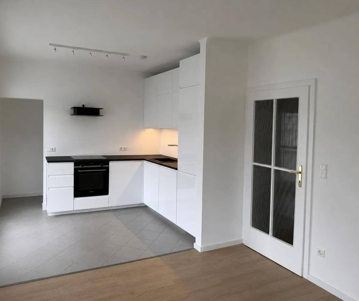 Moderne Einbauküche mit weißen Hochglanzfronten und dunkler Arbeitsplatte in offenem Wohnbereich.