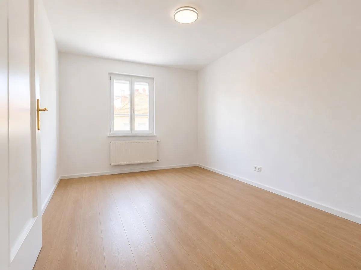 Helles Schlafzimmer mit Parkettboden und einem Fenster, das viel Tageslicht hereinlässt.