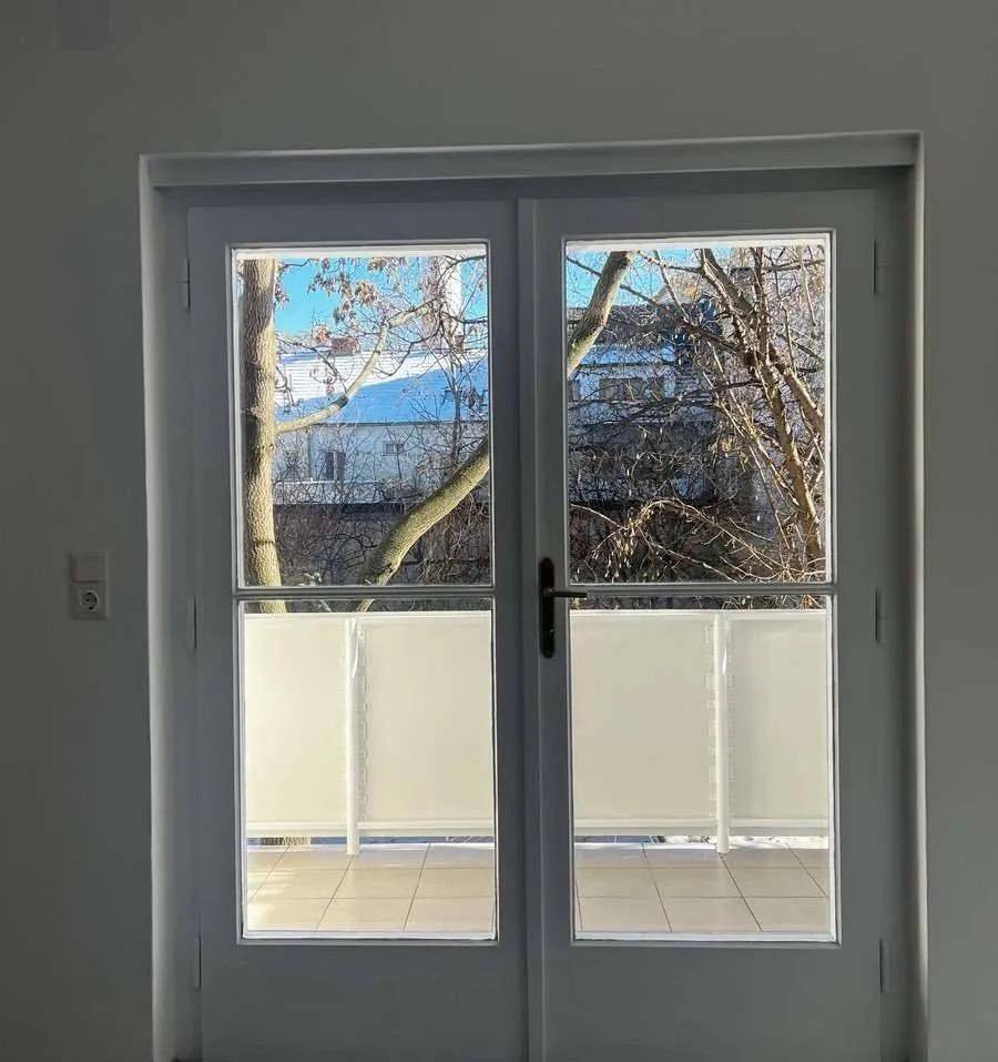 Balkontür mit Blick nach draußen auf den gefliesten Balkon und winterliche Bäume.