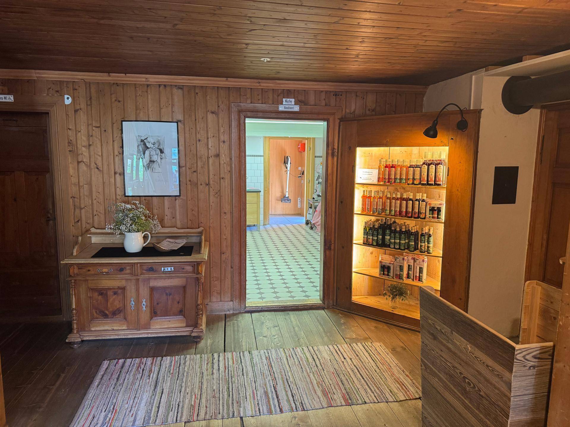 Rustikaler Flur mit Holzvertäfelung, einem antiken Schrank und einem beleuchteten Verkaufsregal.