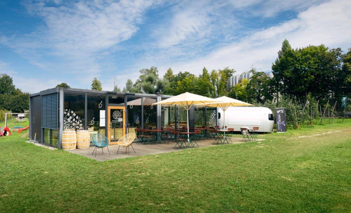 Moderne Außenterrasse mit Sonnenschirmen und Sitzgelegenheiten, umgeben von Grünflächen.