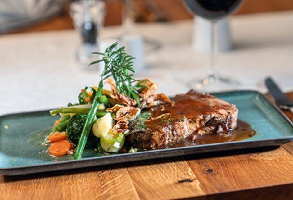 Ein Teller mit Fleisch und Gemüse, ansprechend angerichtet auf einem Holztisch.