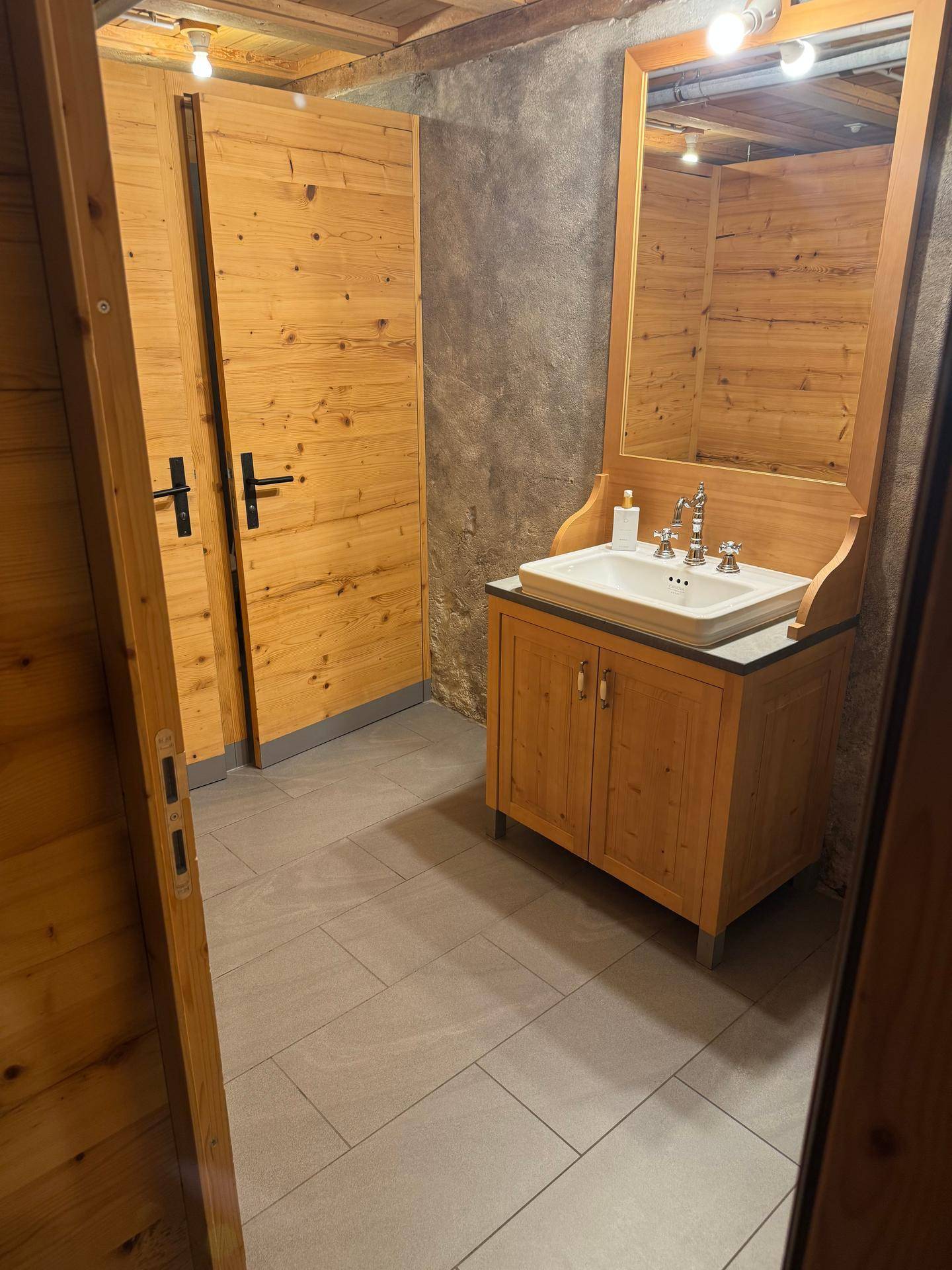 Badezimmer mit Holztüren, einem Holzwaschtisch und modernen grauen Fliesen auf dem Boden.