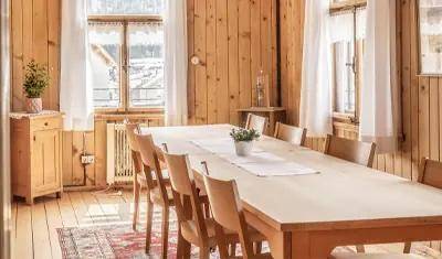 Heller Essbereich mit Holzwänden, langen Holztischen und Stühlen, beleuchtet durch große Fenster.