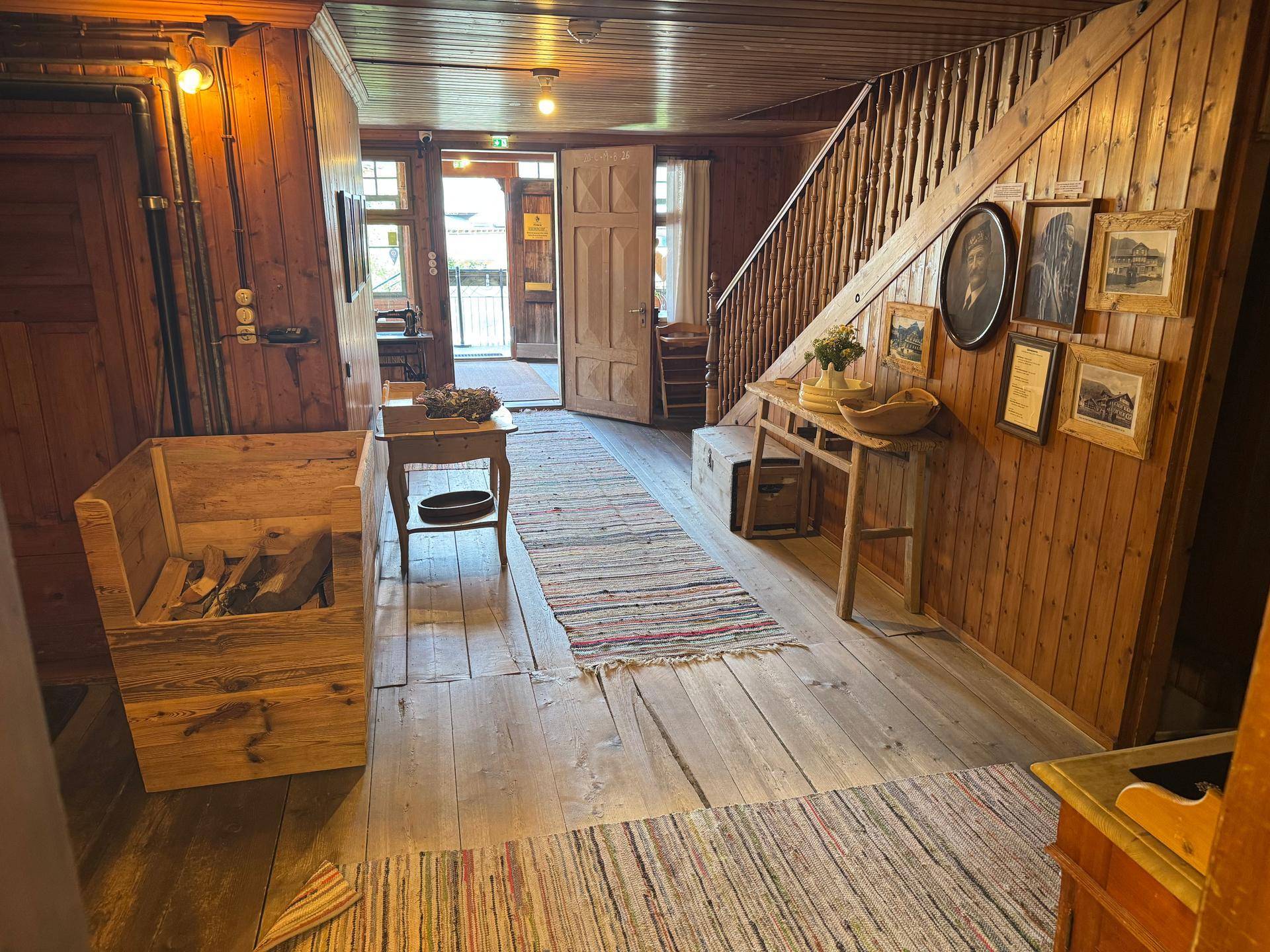 Rustikaler Flur mit Holzböden, Holzvertäfelung und einer Holztreppe, geschmückt mit alten Bildern.