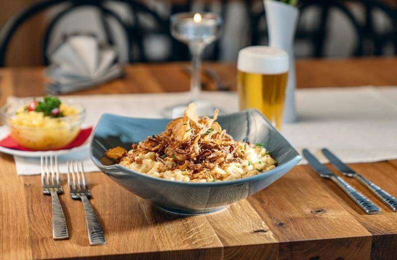 Eine Schüssel Käsespätzle mit Röstzwiebeln auf einem Holztisch, festlich gedeckt.
