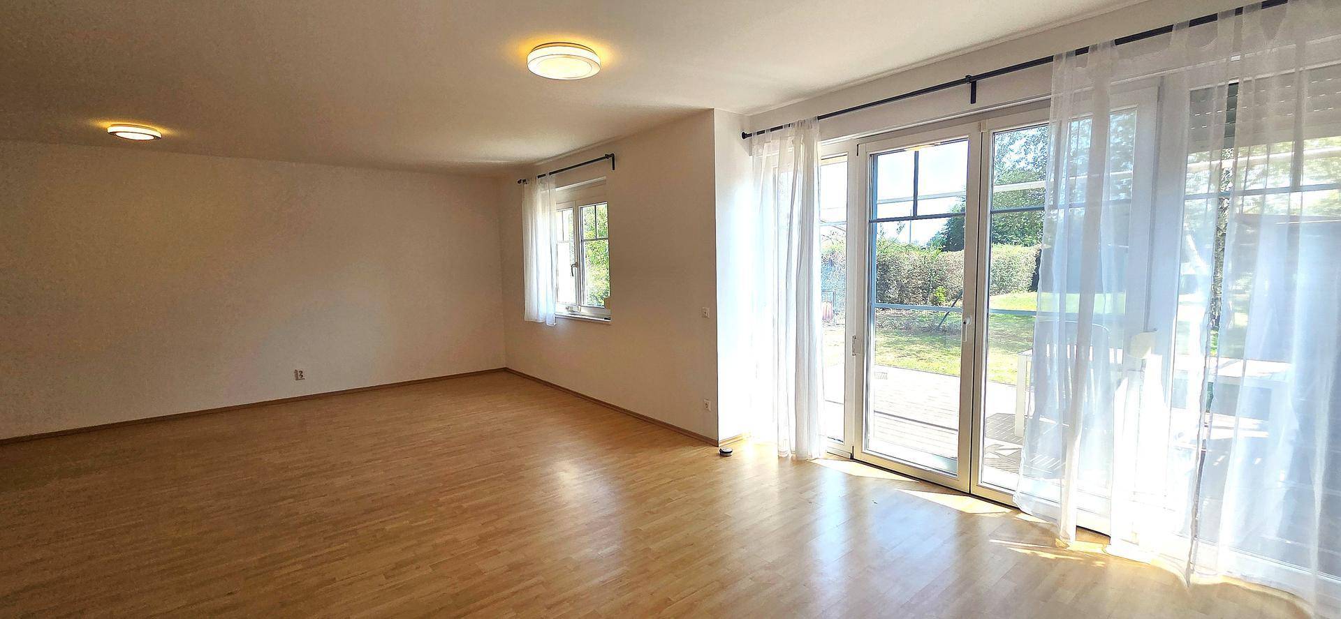 Lichtdurchflutetes Wohnzimmer mit Laminatboden und großen Fenstern zum Garten.