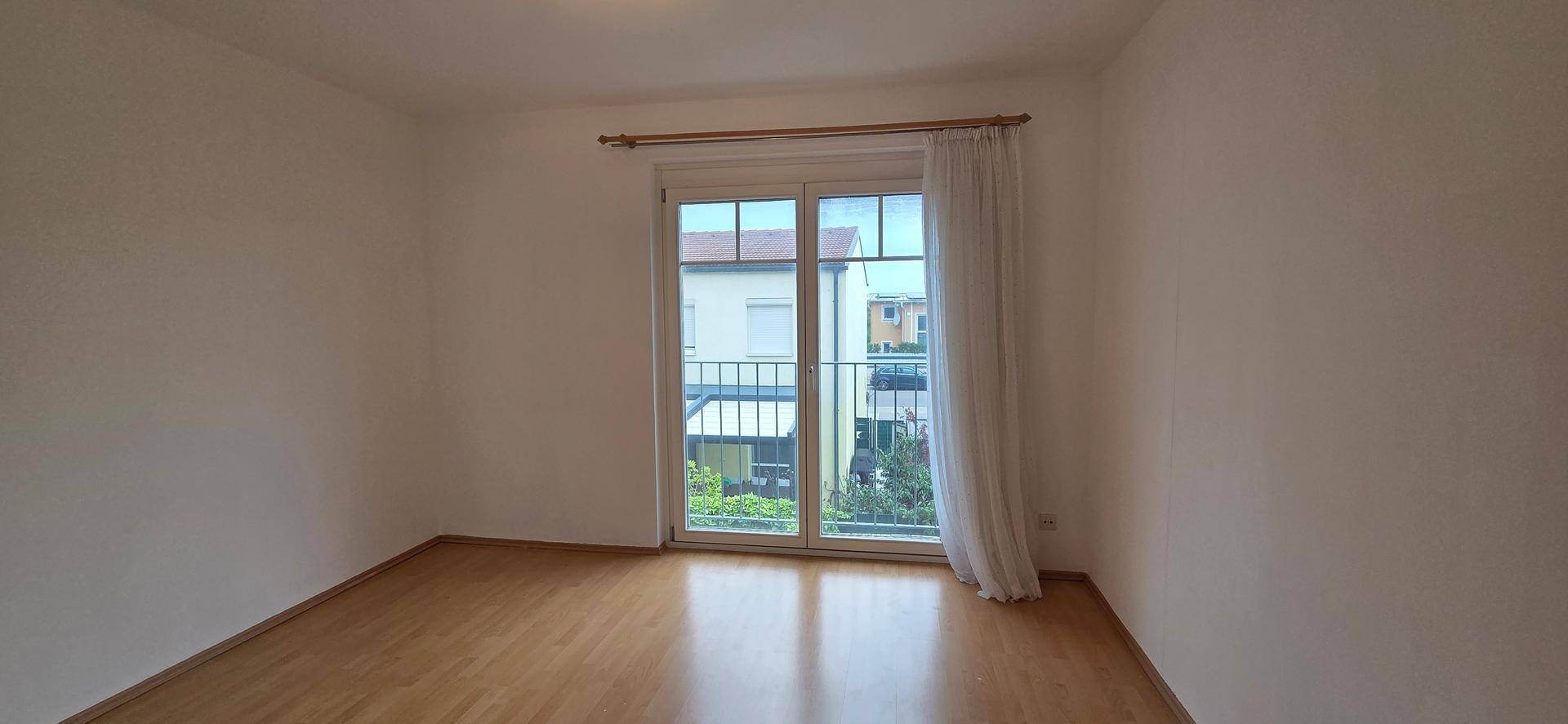 Schlafzimmer mit Laminatboden und Zugang zu einem französischen Balkon mit Blick ins Grüne.